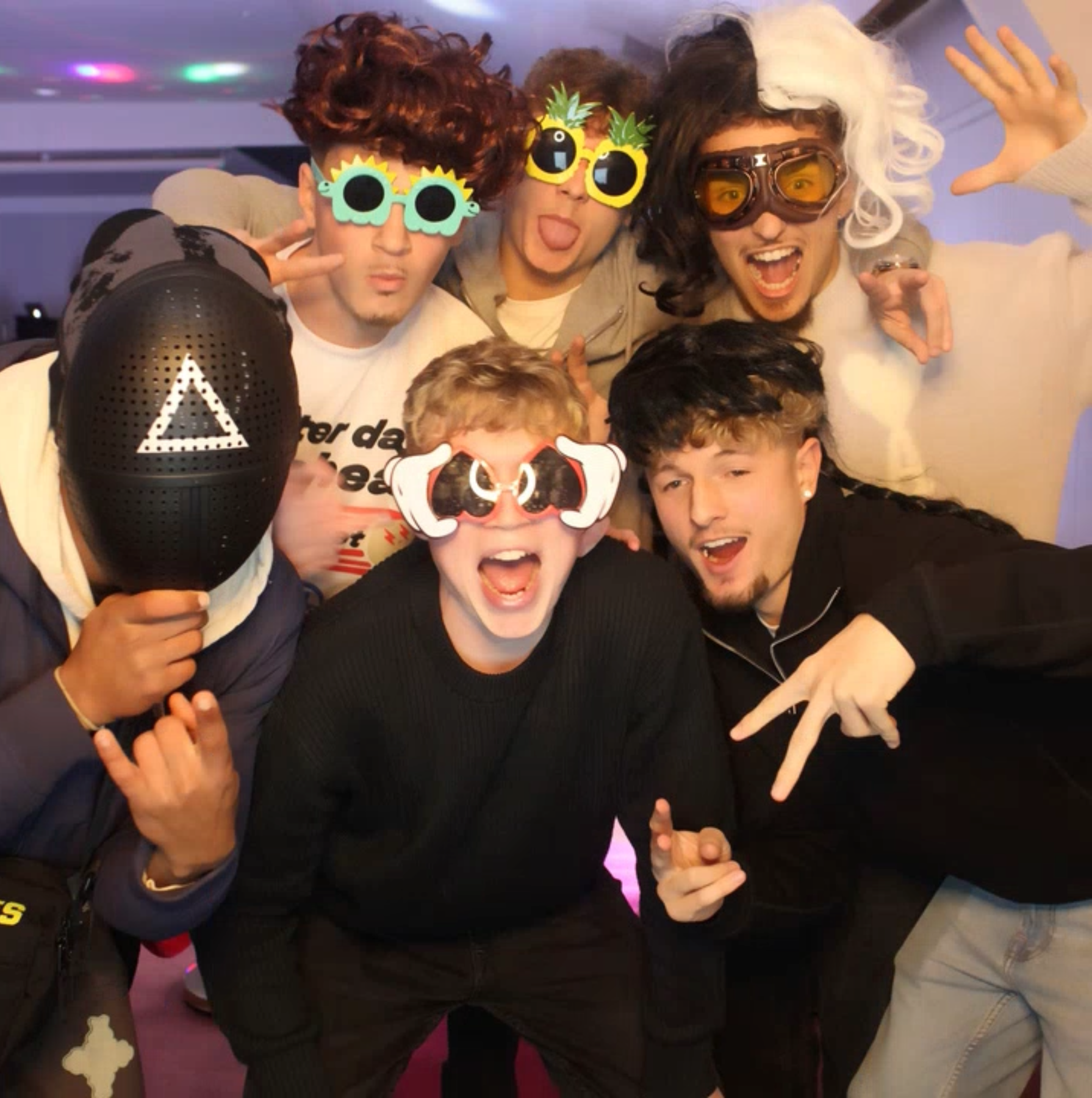 Playful photo booth at a lively party, five friends in funky glasses pose under pink-purple lights with cheerful, high-energy vibes.