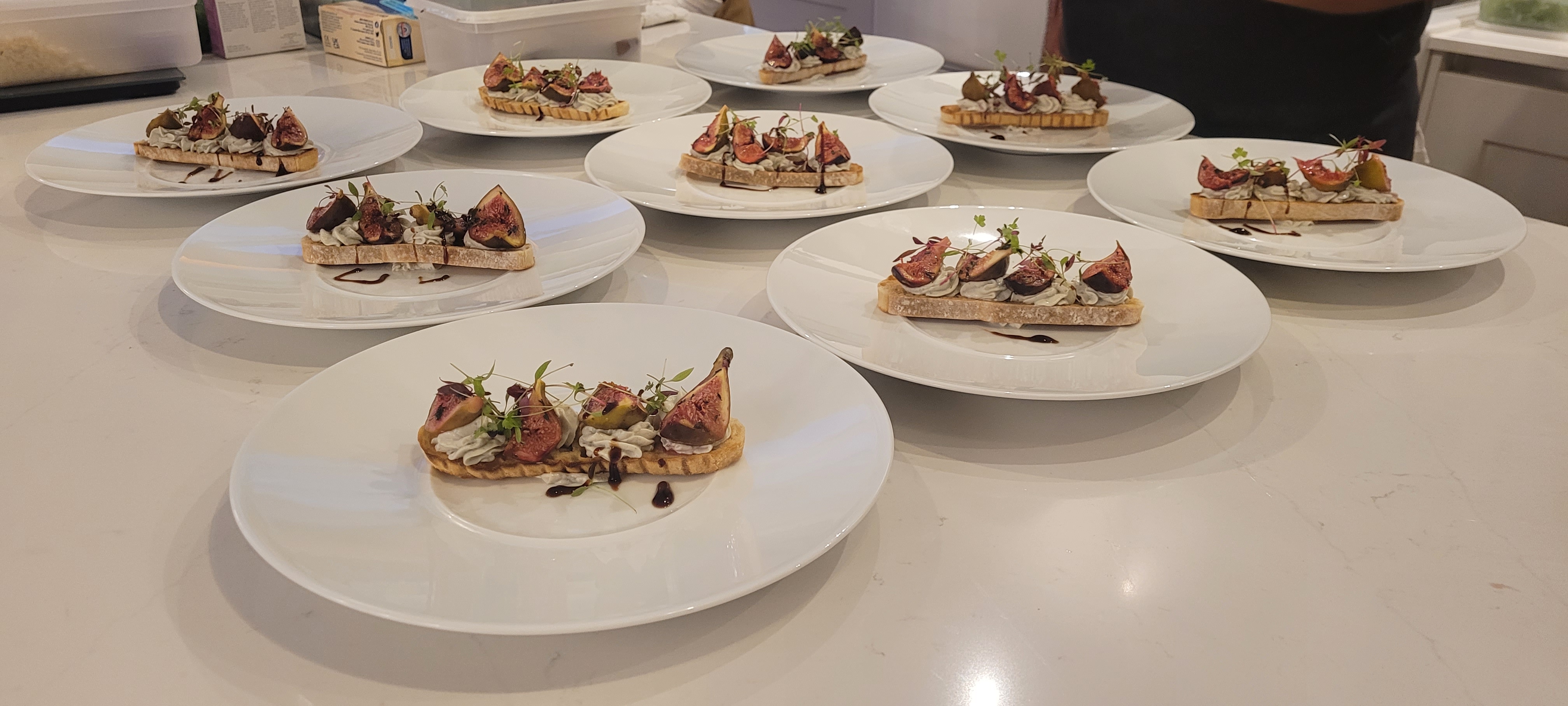 Artfully arranged on minimalist white plates, these gourmet dishes feature crisp toast topped with creamy filling, figs, and microgreens, exuding elegance.