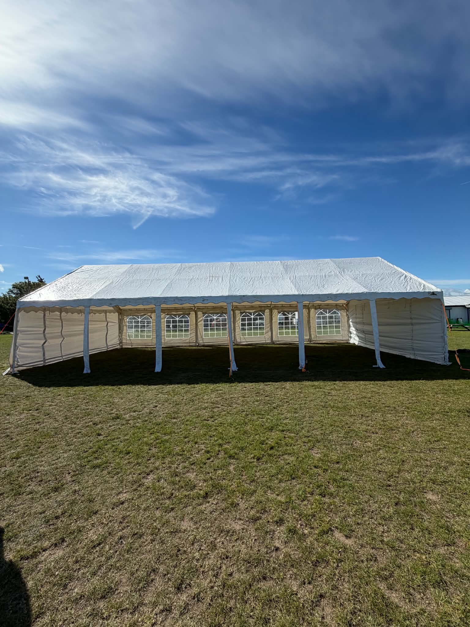 Large white event tent on a grassy field, with clear arched windows and crisp poles under bright blue daylight, ideal for catering.
