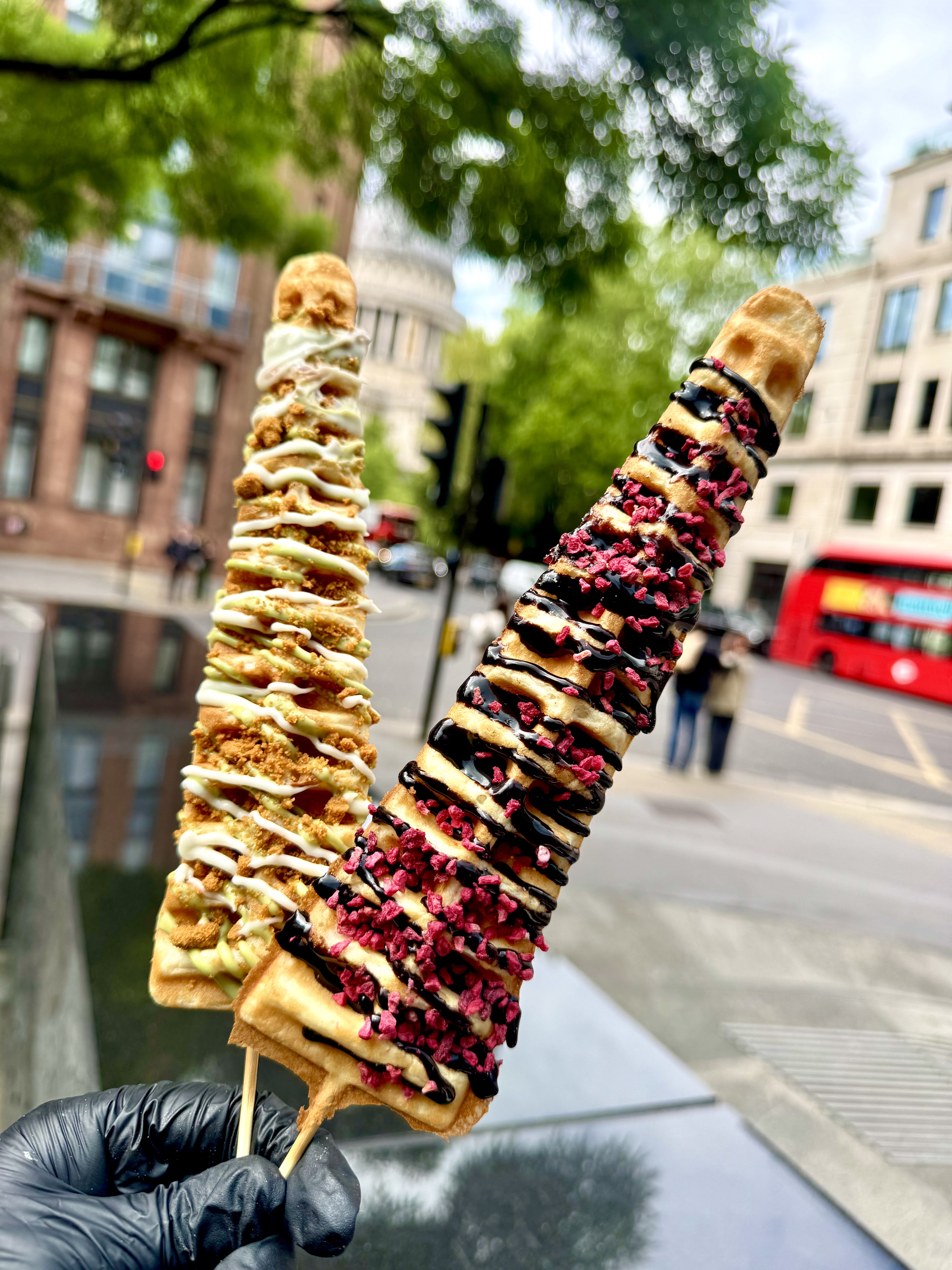 Colorful waffle sticks drizzled with sauces and sprinkles are held up in sunny outdoor festivities, highlighting vibrant Caribbean vibes.