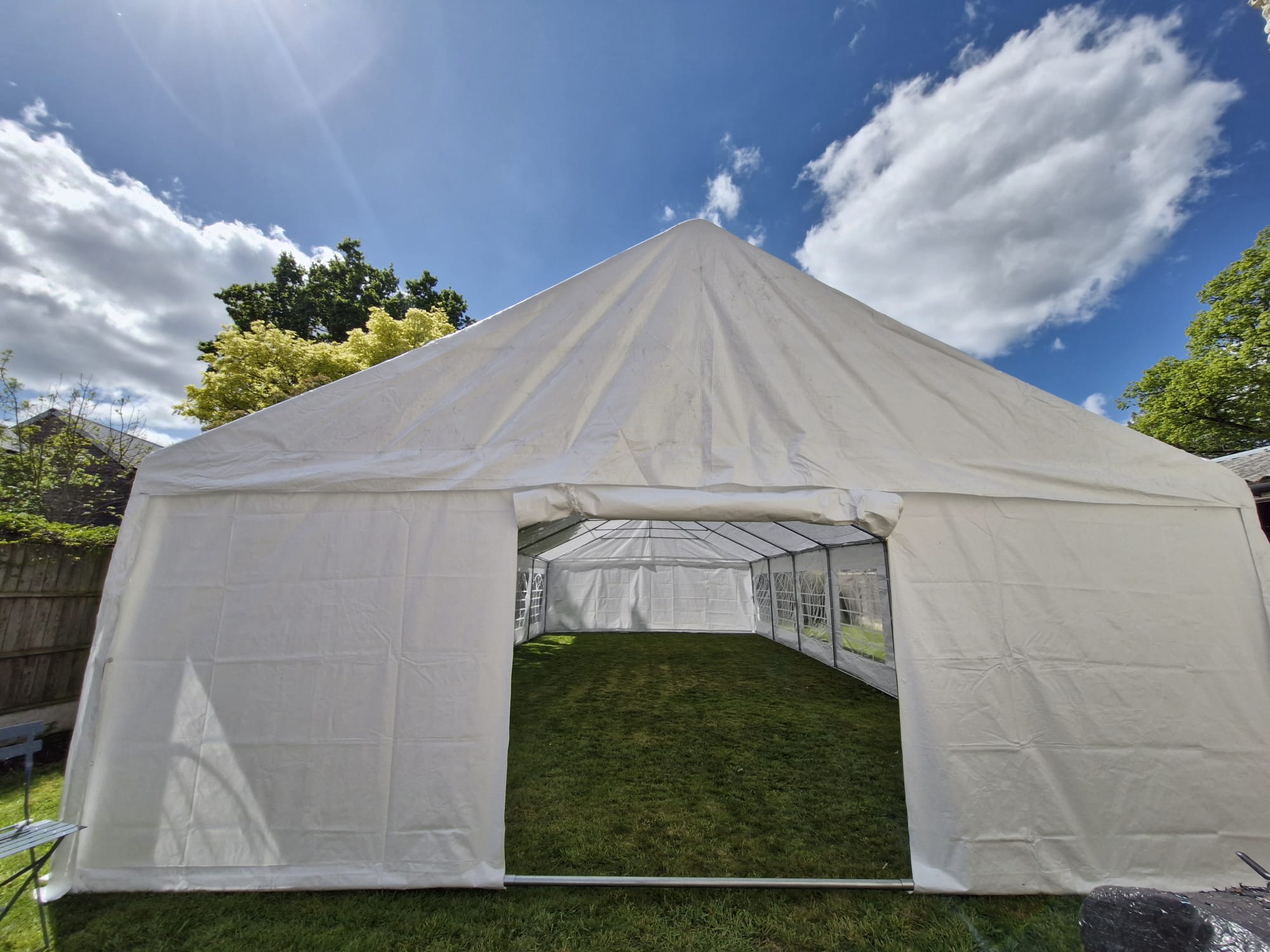 Bright daylight over a white marquee tent on grass, open entrance, clear side panels, and crisp setup for outdoor catering.