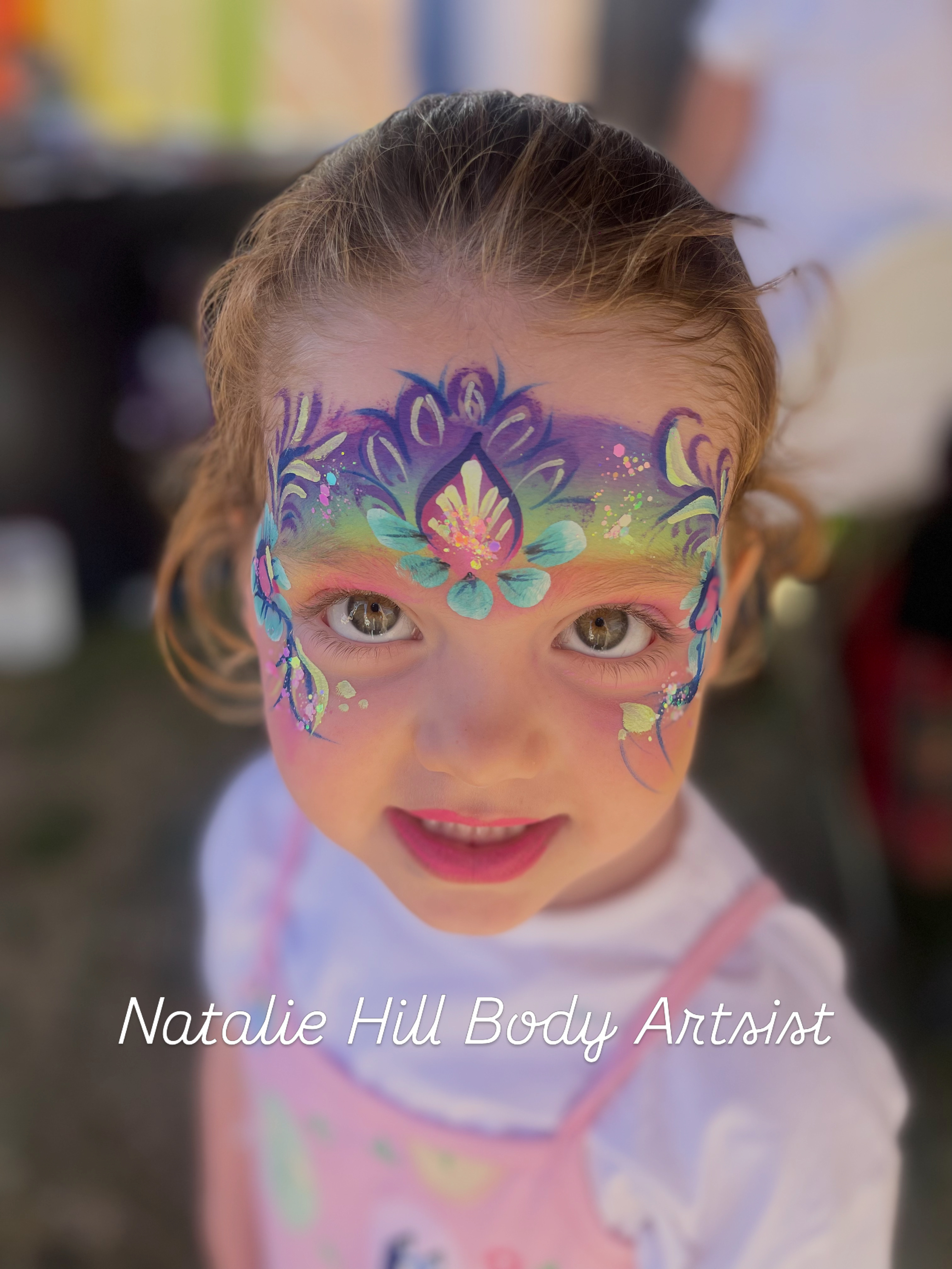 A vibrant face painting features bold colors like pink, yellow, and white, accentuating the model’s striking expression against a dark backdrop.