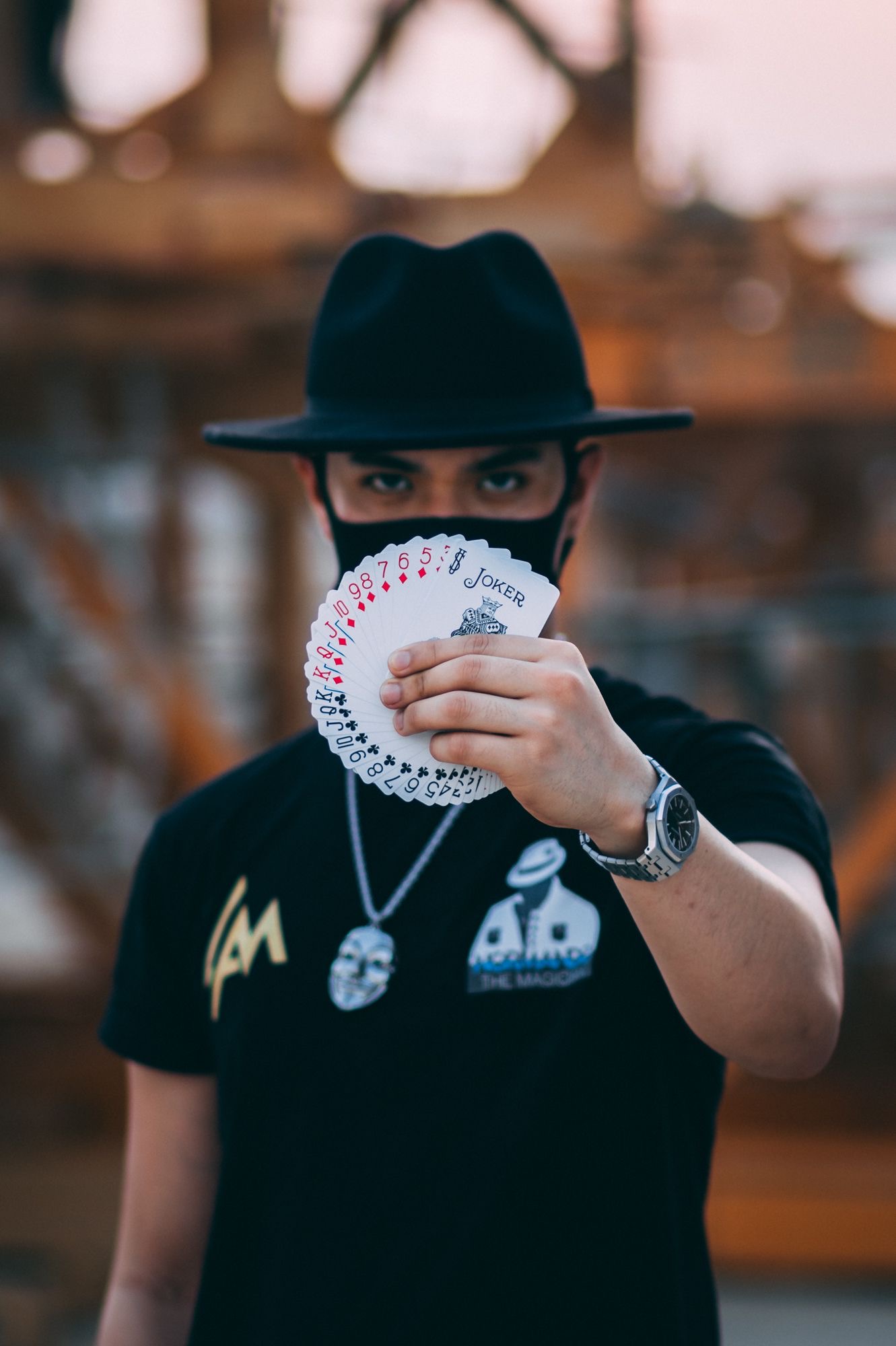 A magician holds a fan of playing cards, showcasing intricate designs, amidst a warm sunset backdrop, exuding mystery and charm.
