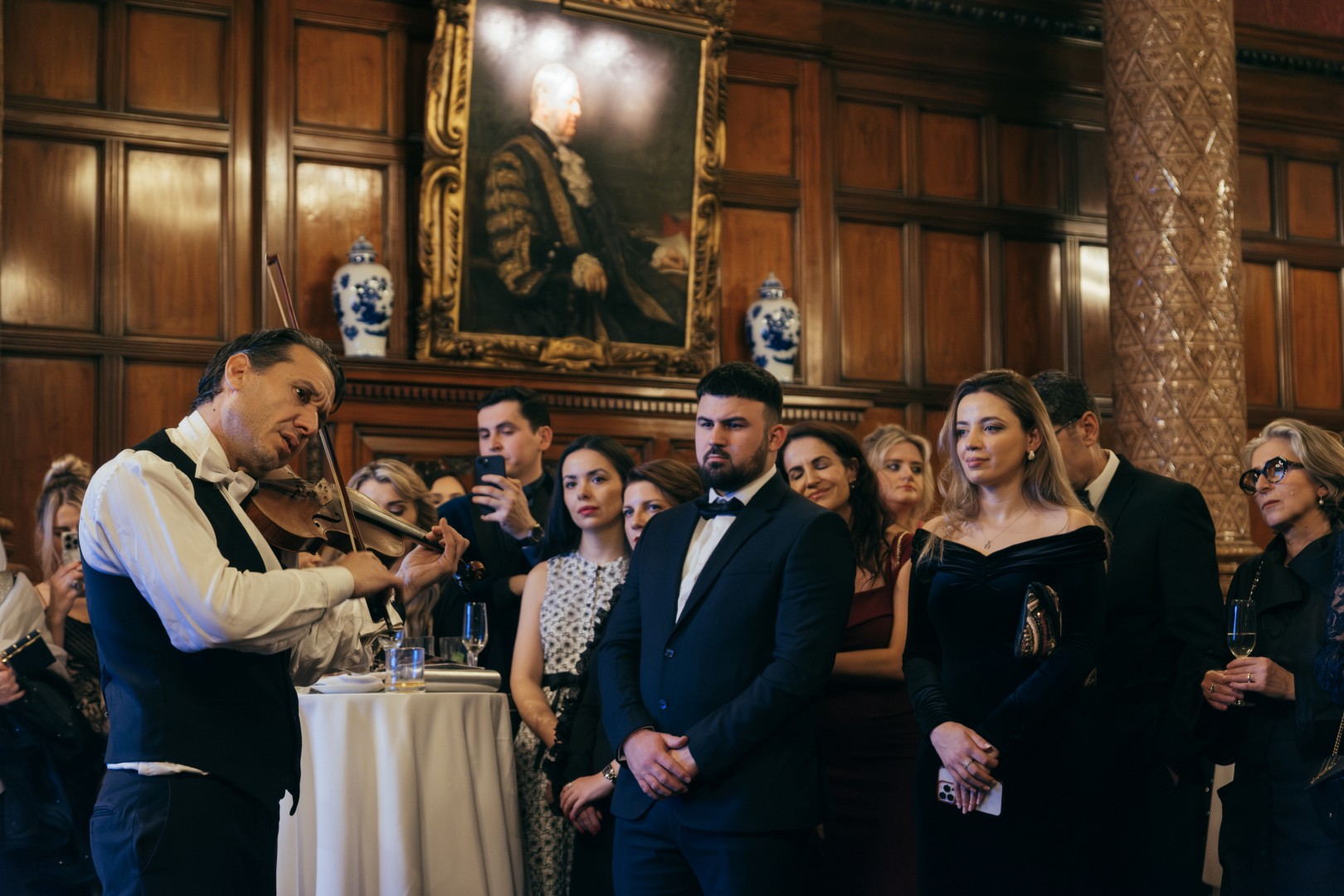 A violinist captivates a stylish crowd in formal attire against rich wood paneling and elegant decor, creating a sophisticated atmosphere.