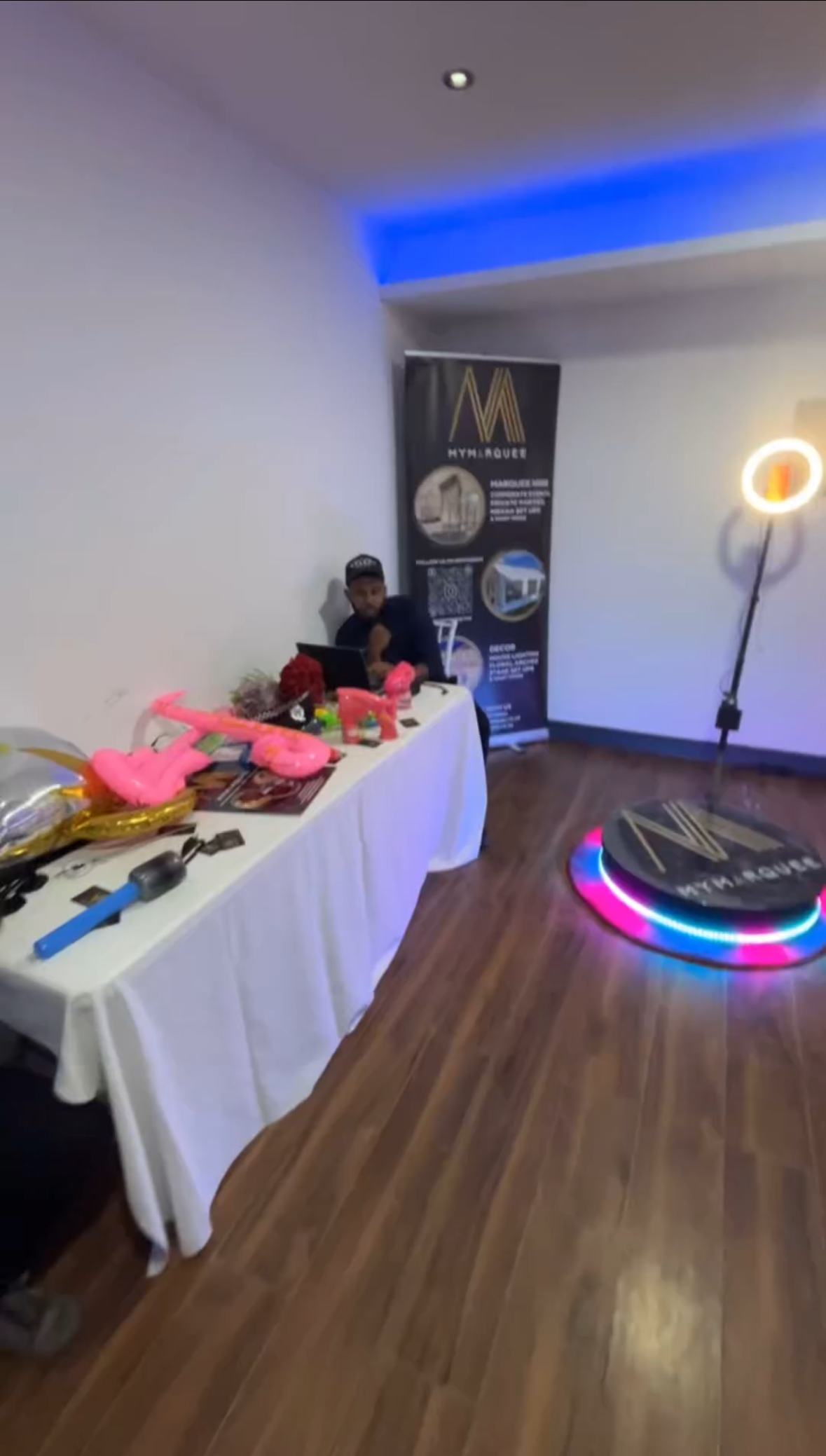A vibrant setup features a table adorned with pink inflatable guitars and party supplies, complemented by a lit ring backdrop, enhancing a festive atmosphere.