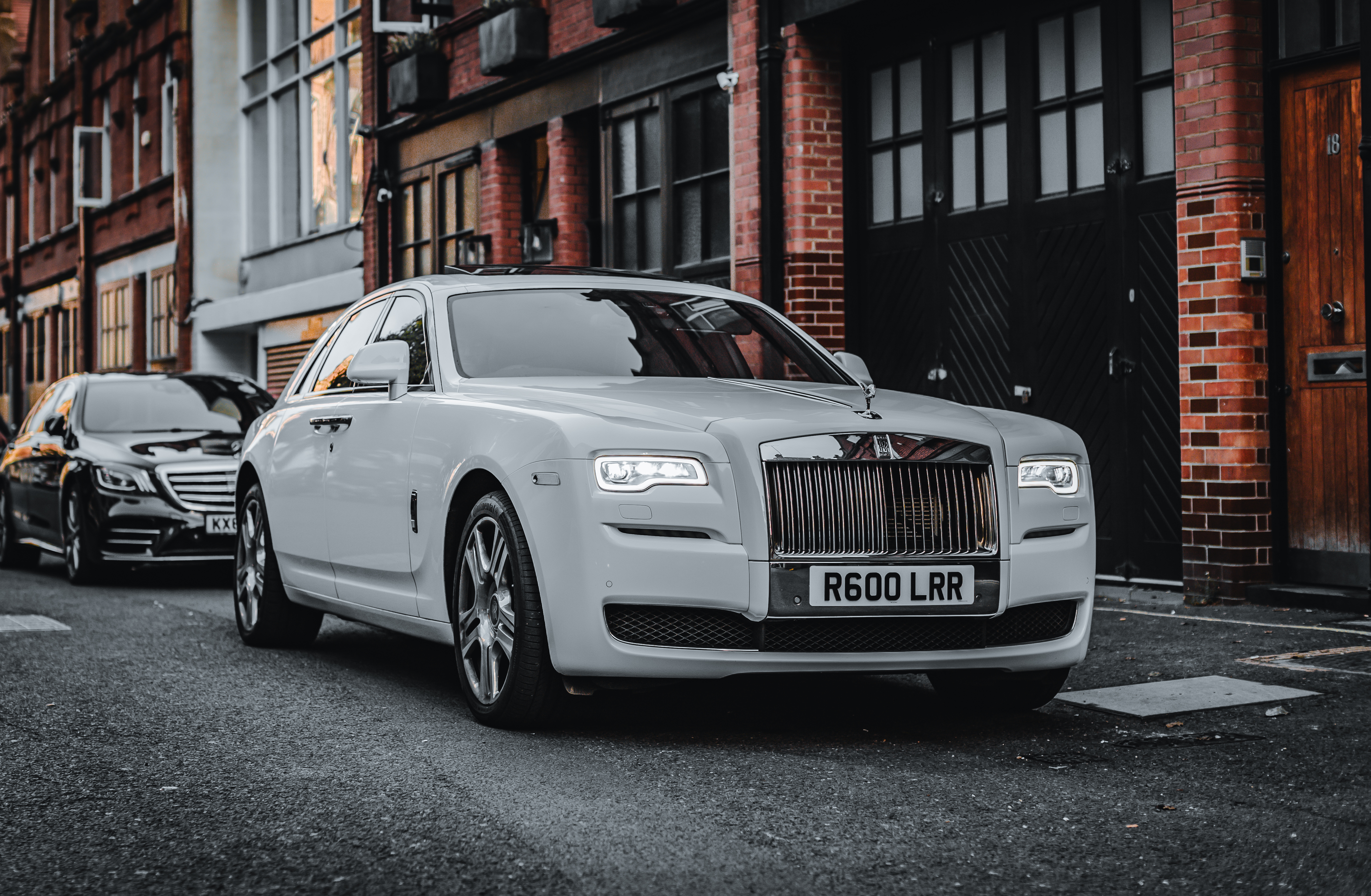 A luxurious white Rolls-Royce parked alongside a sleek black sedan, framed by brick buildings, creating a refined urban atmosphere.