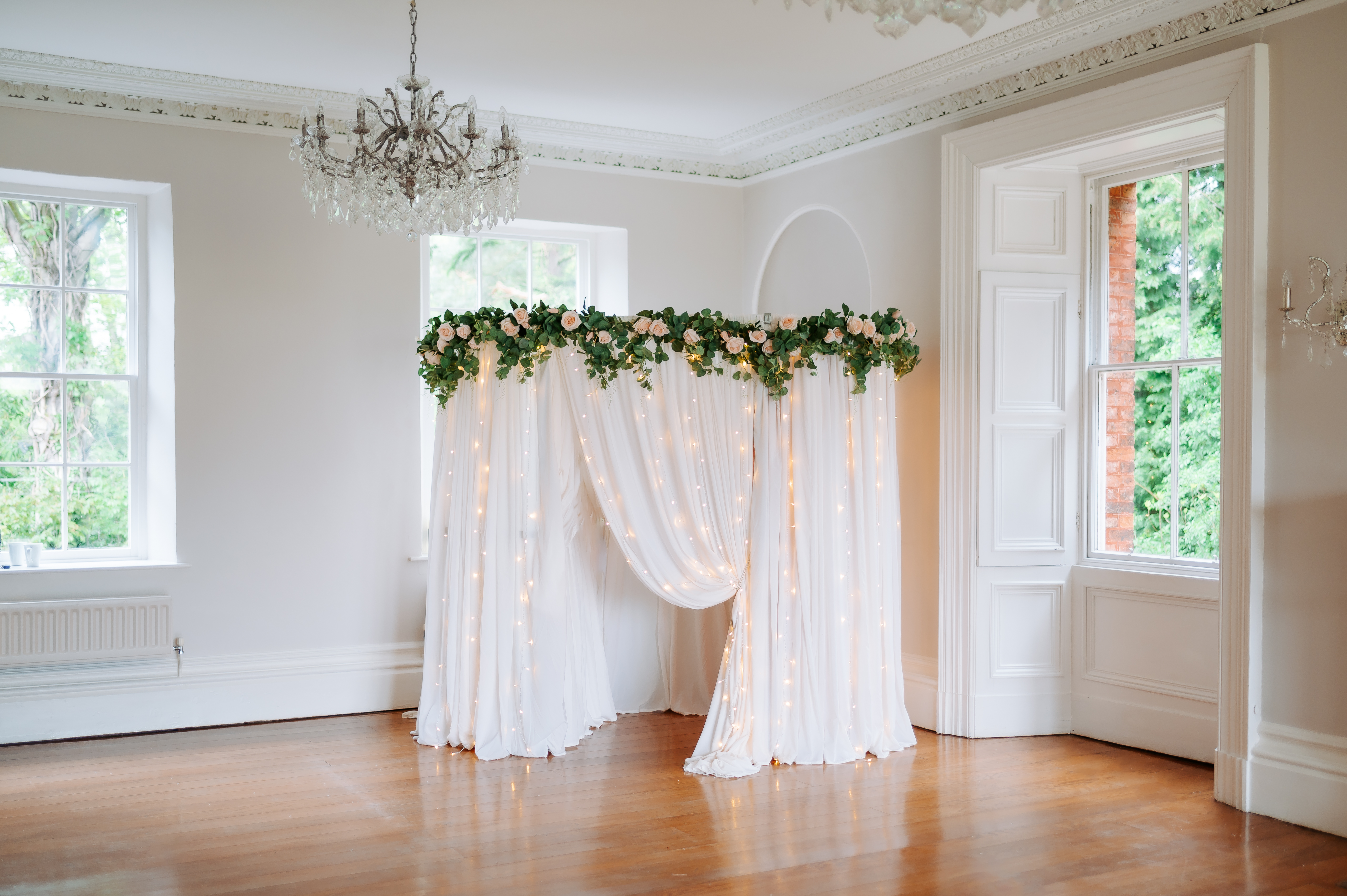 The elegant venue features round tables with crisp white linens, adorned with floral centerpieces, amid warm ambient lighting and rustic wooden beams.