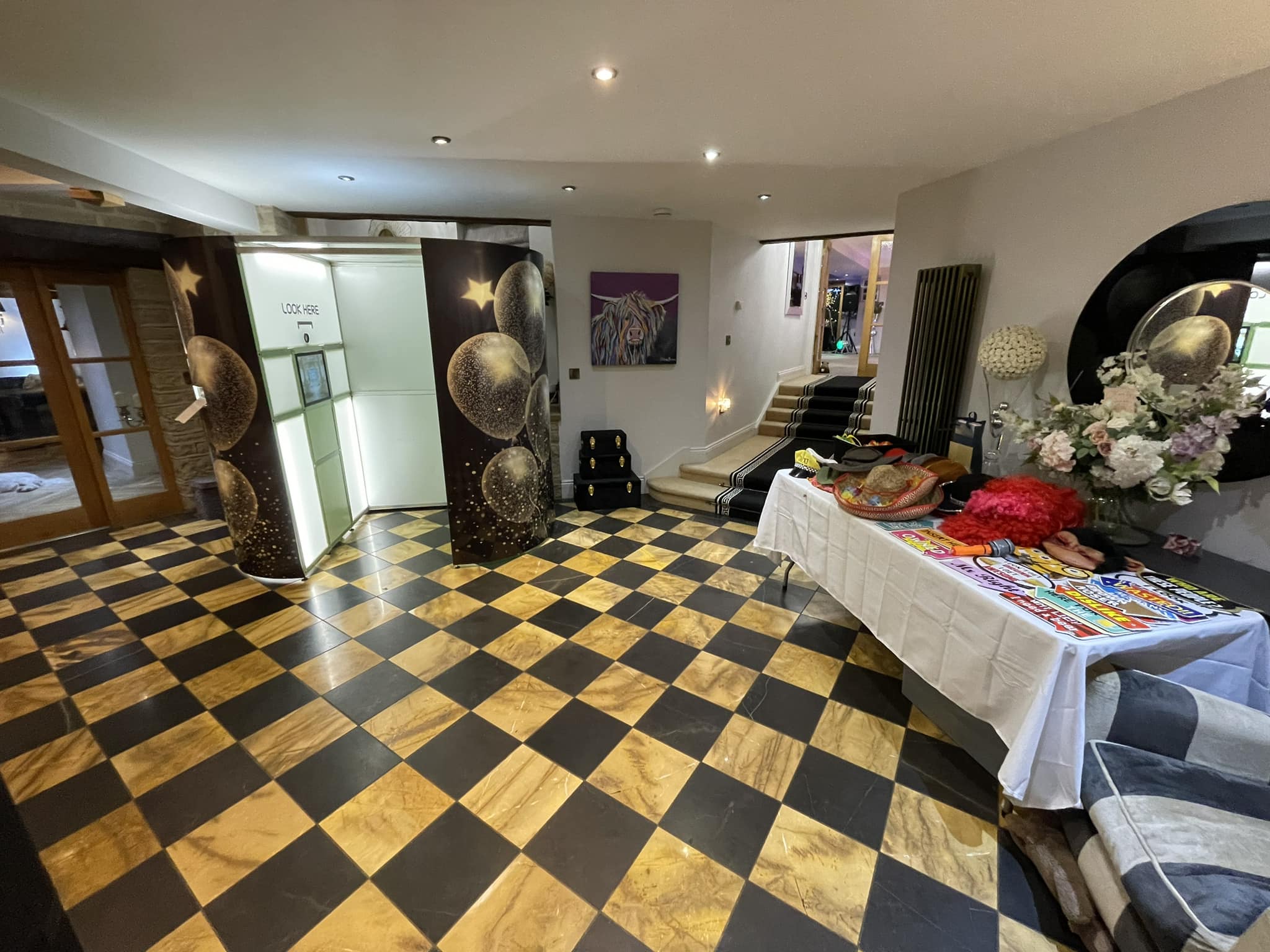 Inside a stylish entryway, a striking black and gold checkered floor complements a white table adorned with vibrant hats and props, exuding a festive vibe.