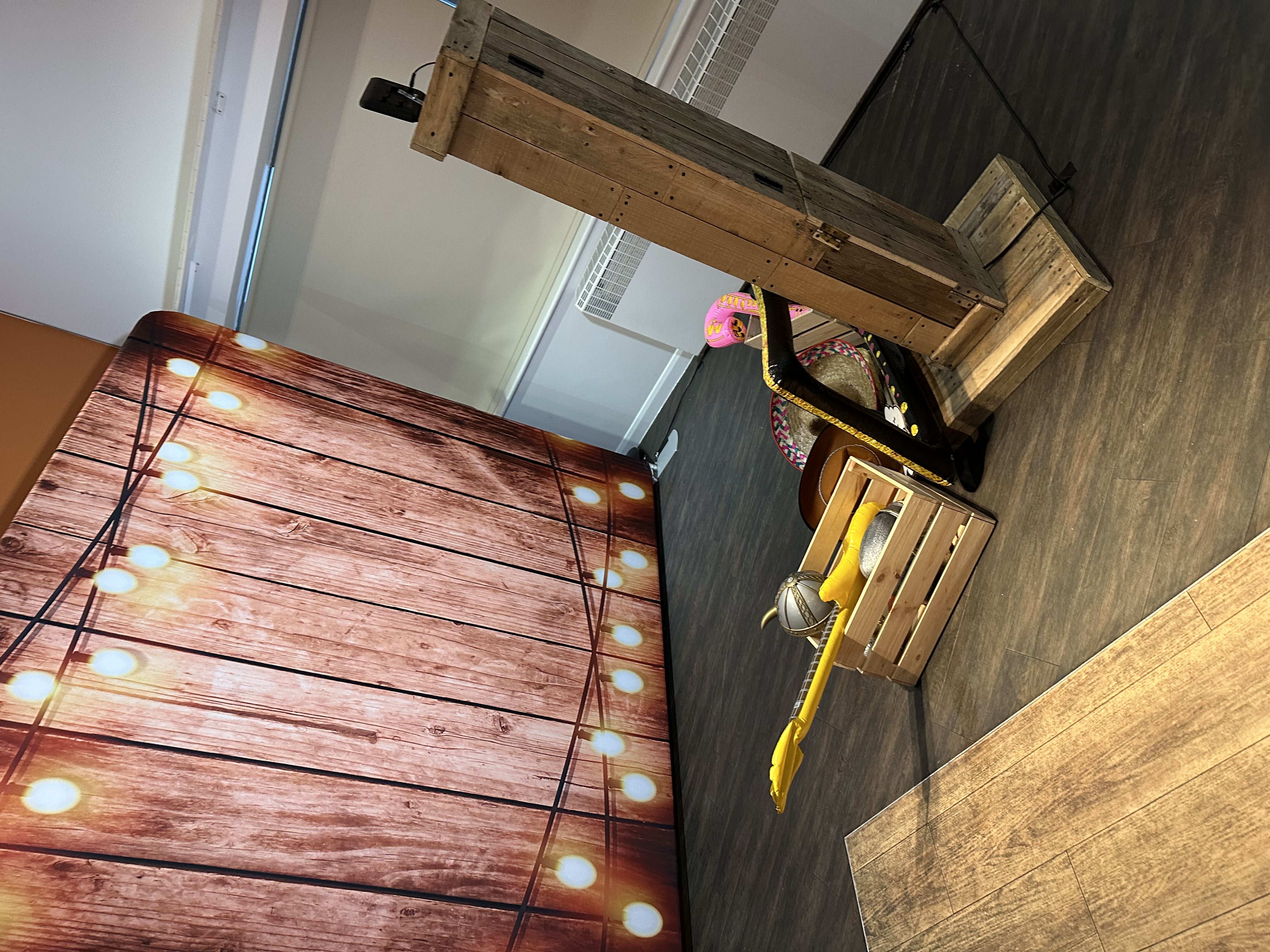 A cozy event space features a wooden backdrop adorned with glowing string lights, a wooden crate filled with bright toy instruments, and rustic decor, all set in warm lighting for a vibrant atmosphere.