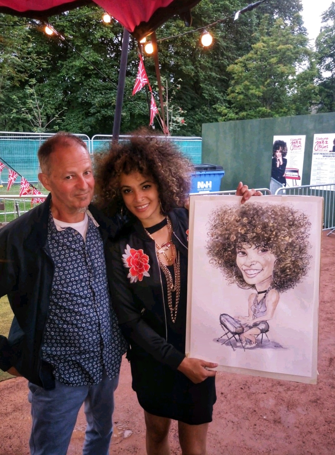 A joyful couple stands next to a colorful caricature, framed on a rustic wood display; warm lighting enhances their celebratory mood.
