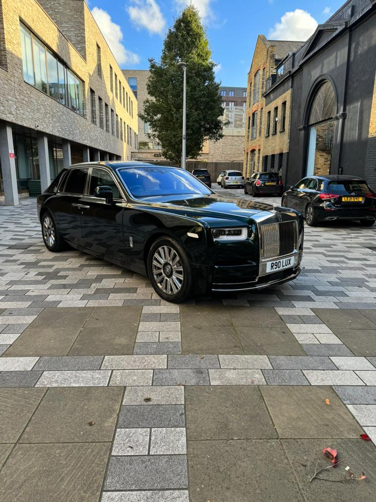 A luxurious black Rolls Royce parks elegantly on a patterned gray stone plaza, framed by modern buildings under bright daylight.