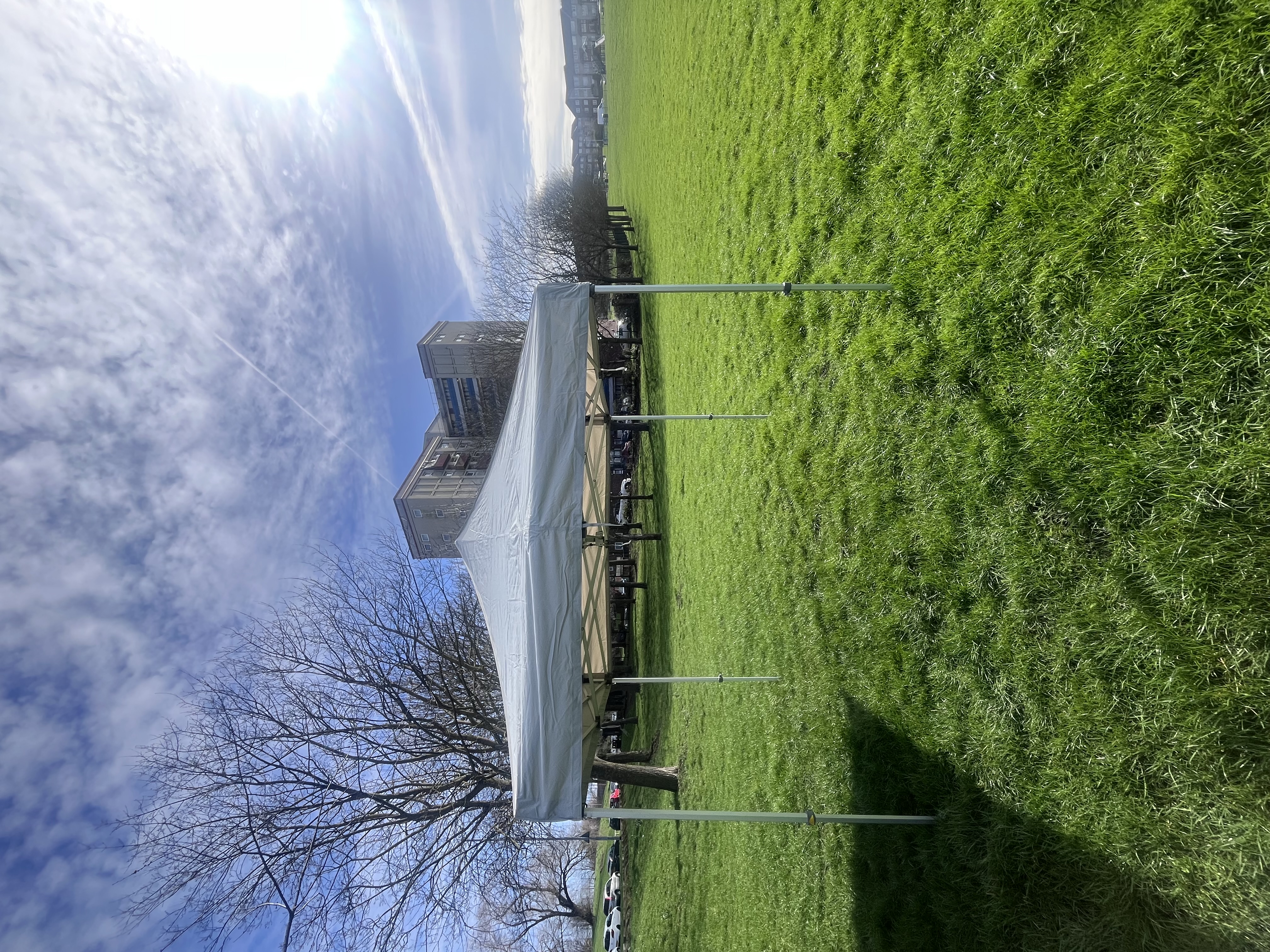 A white canopy tent stands on vibrant green grass under a bright, sunny sky, perfect for outdoor catering events in a lively park.