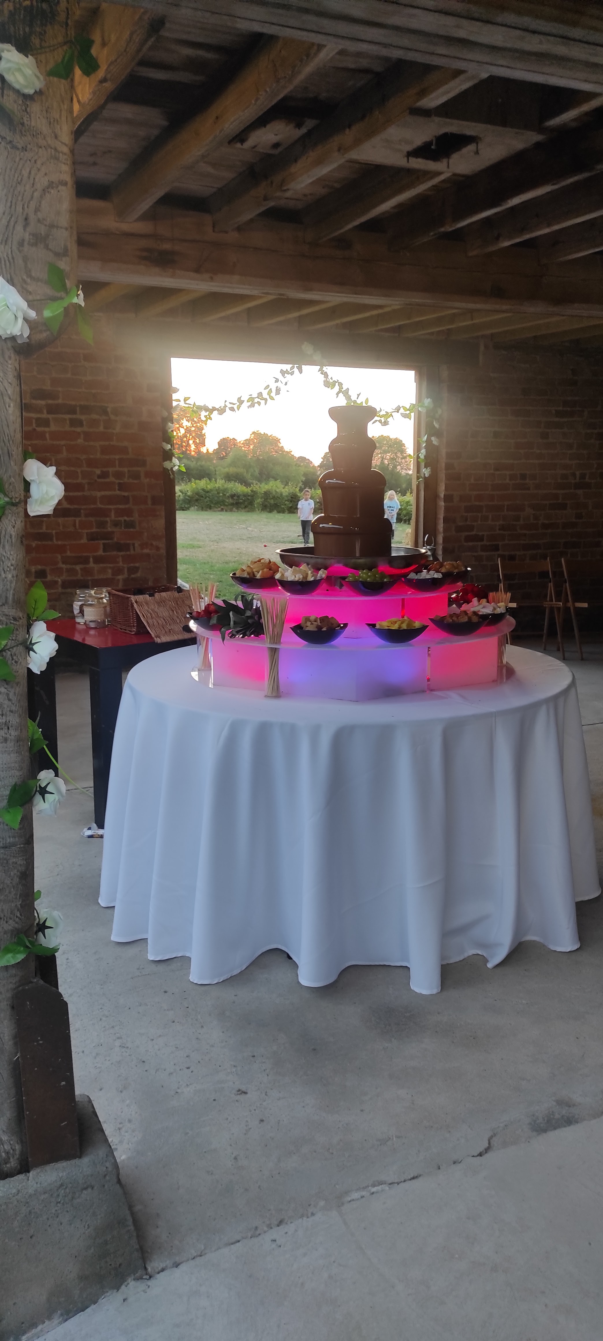 A vibrant chocolate fountain centerpiece with colorful fruit platters is surrounded by crisp white linens, evoking a cheerful catering vibe.