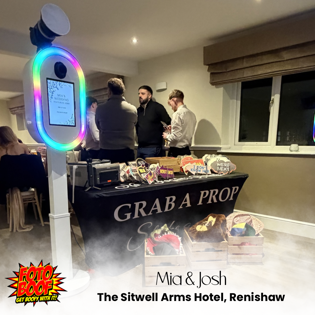 At The Sitwell Arms, a vibrant photo booth features colorful props on a sleek black table. Guests mingle in soft, warm lighting, creating a festive atmosphere.