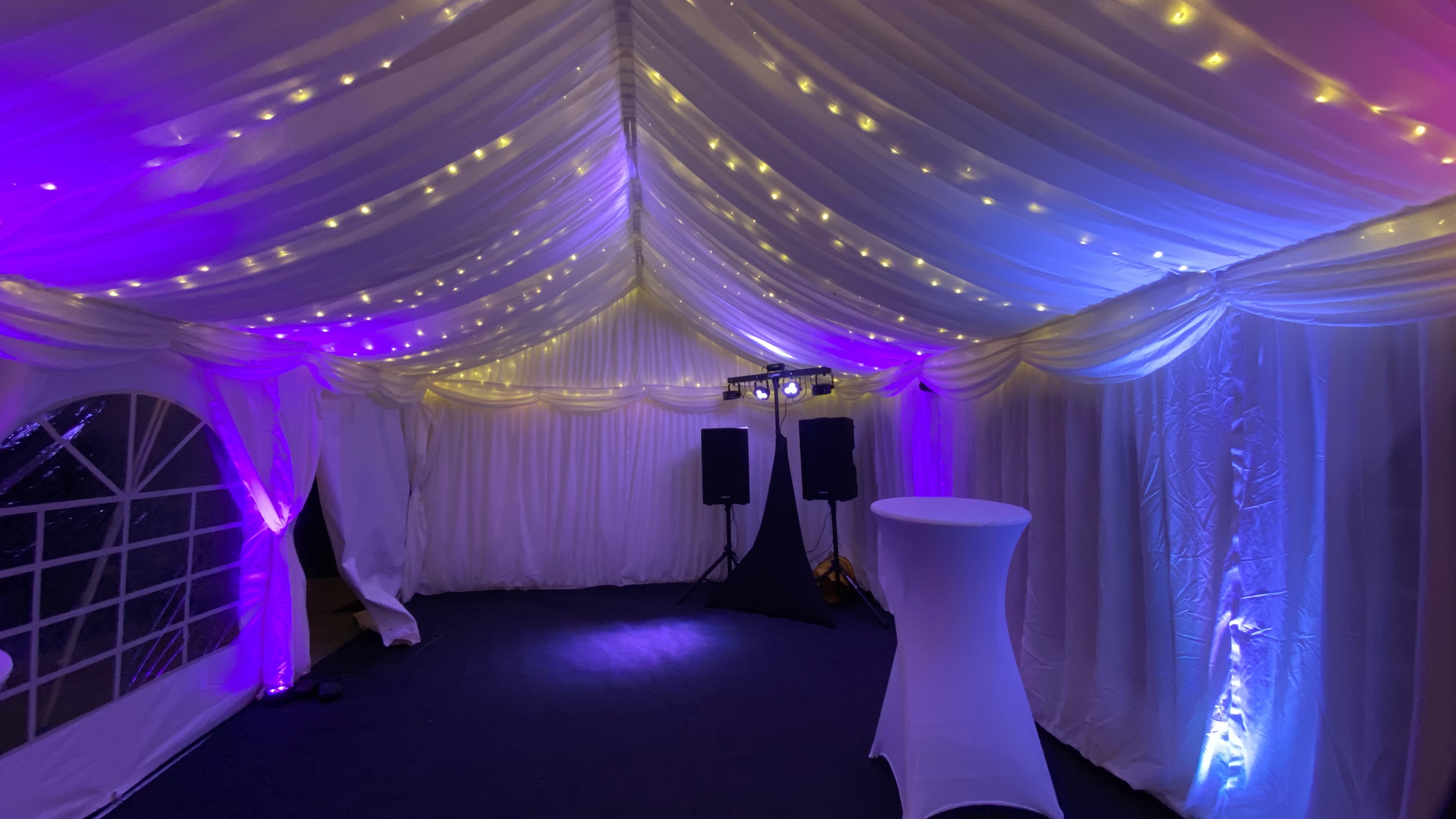 A romantic marquee features soft white draping and twinkling fairy lights, creating a cozy vibe with purple and golden hues, ideal for events.