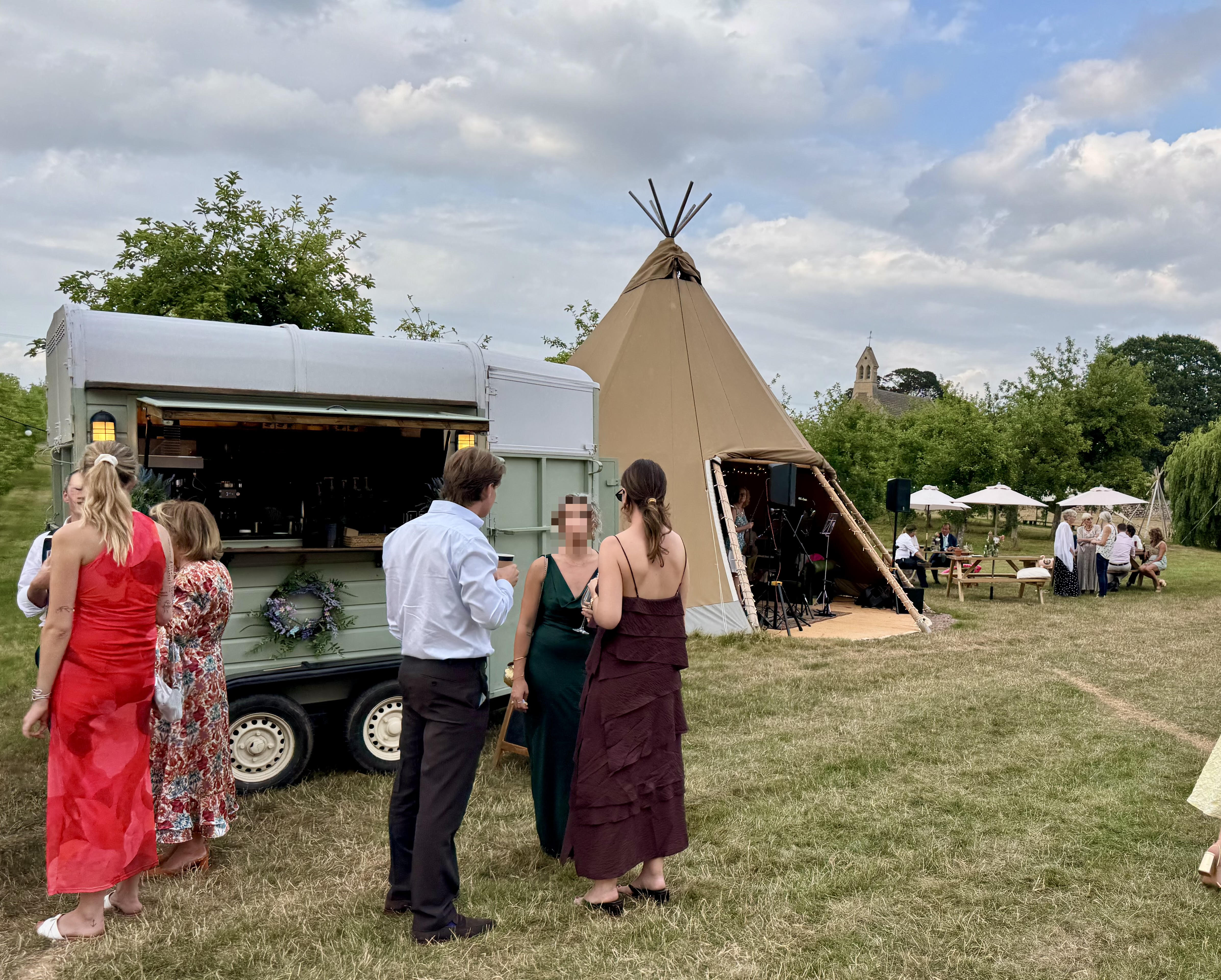 Elegant outdoor catering scene with a vintage van bar and beige teepee tent, guests mingling on grass under soft daylight.