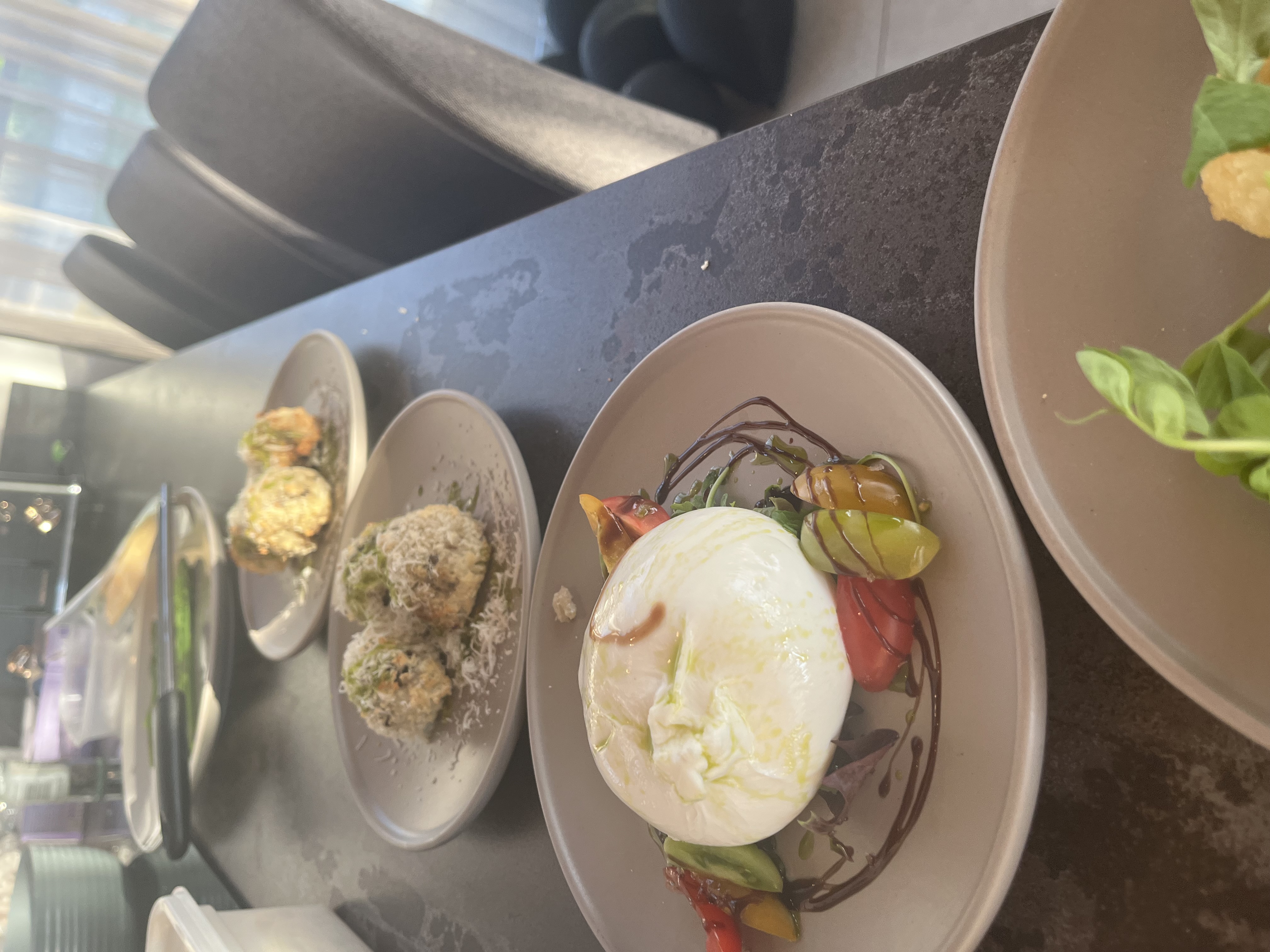 Elegant catering buffet on a dark stone counter with caprese, fried bites, and polished beige plates in warm daylight.