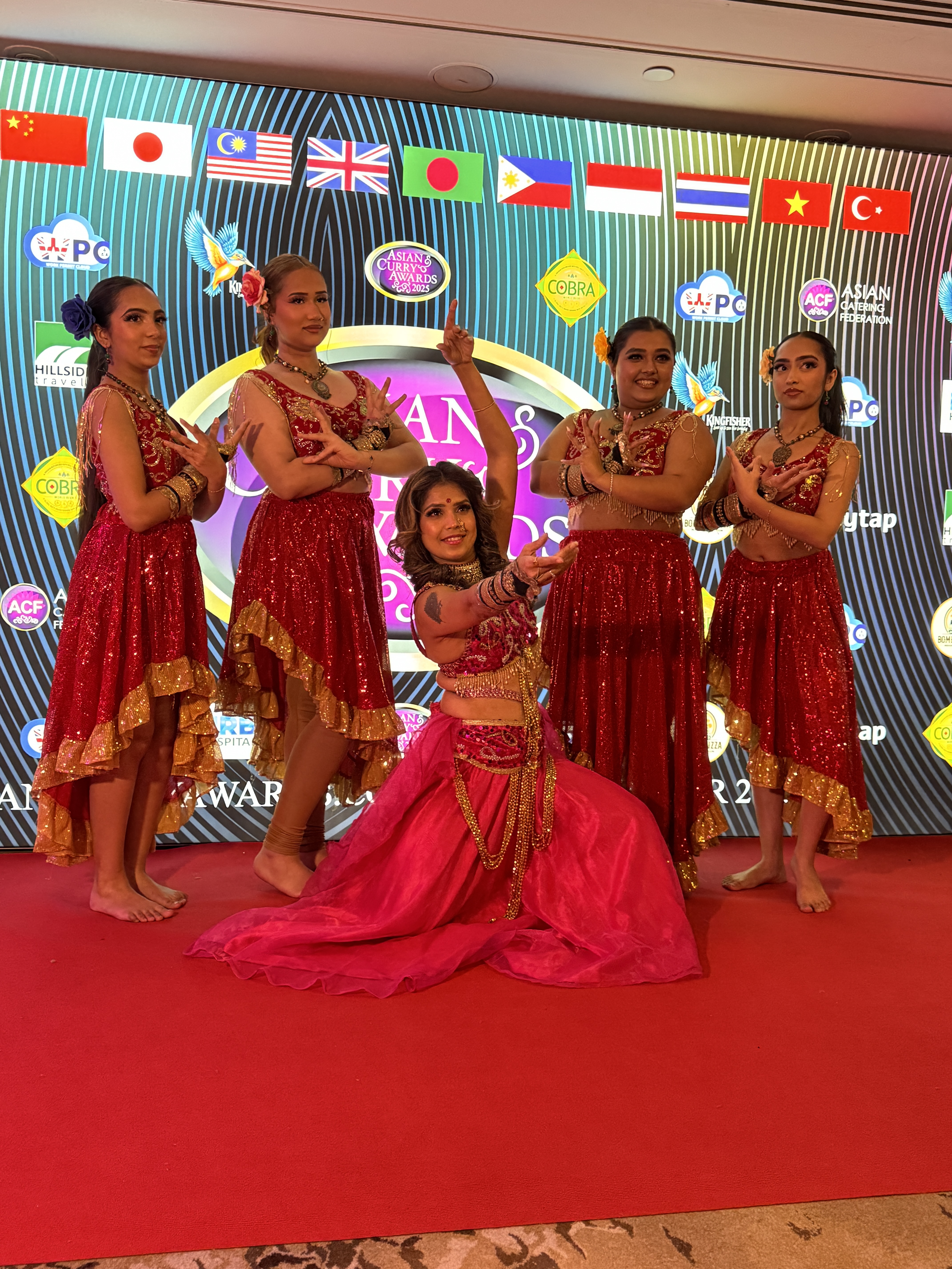 Vibrant dancers in colorful outfits of green and pink gracefully perform on a glossy white dance floor, surrounded by elegant decor and soft lighting.