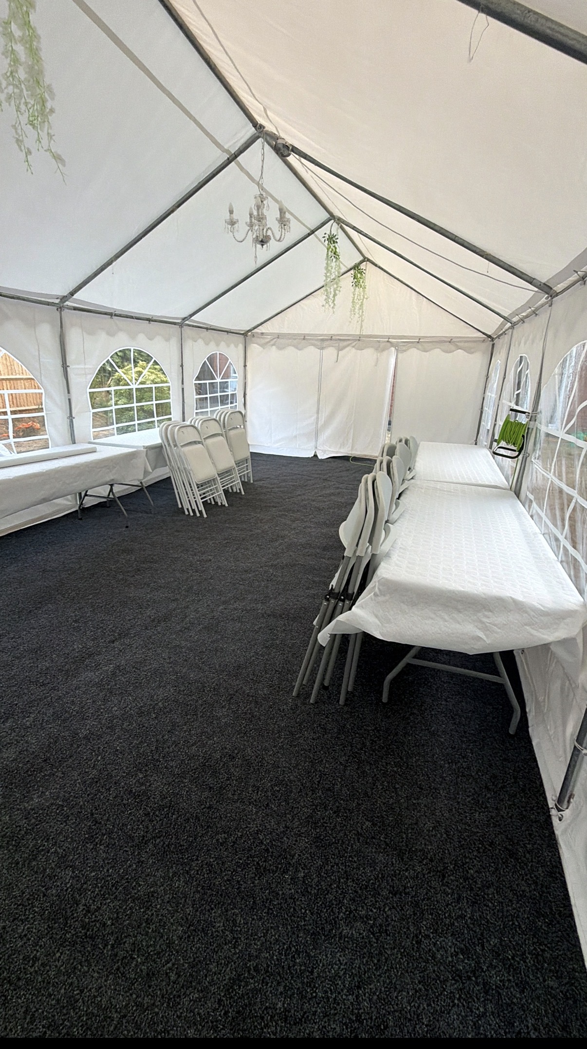 Bright daylight inside a clean white event tent, with banquet tables, stacked folding chairs, dark carpet, chandeliers, and a polished catering setup.