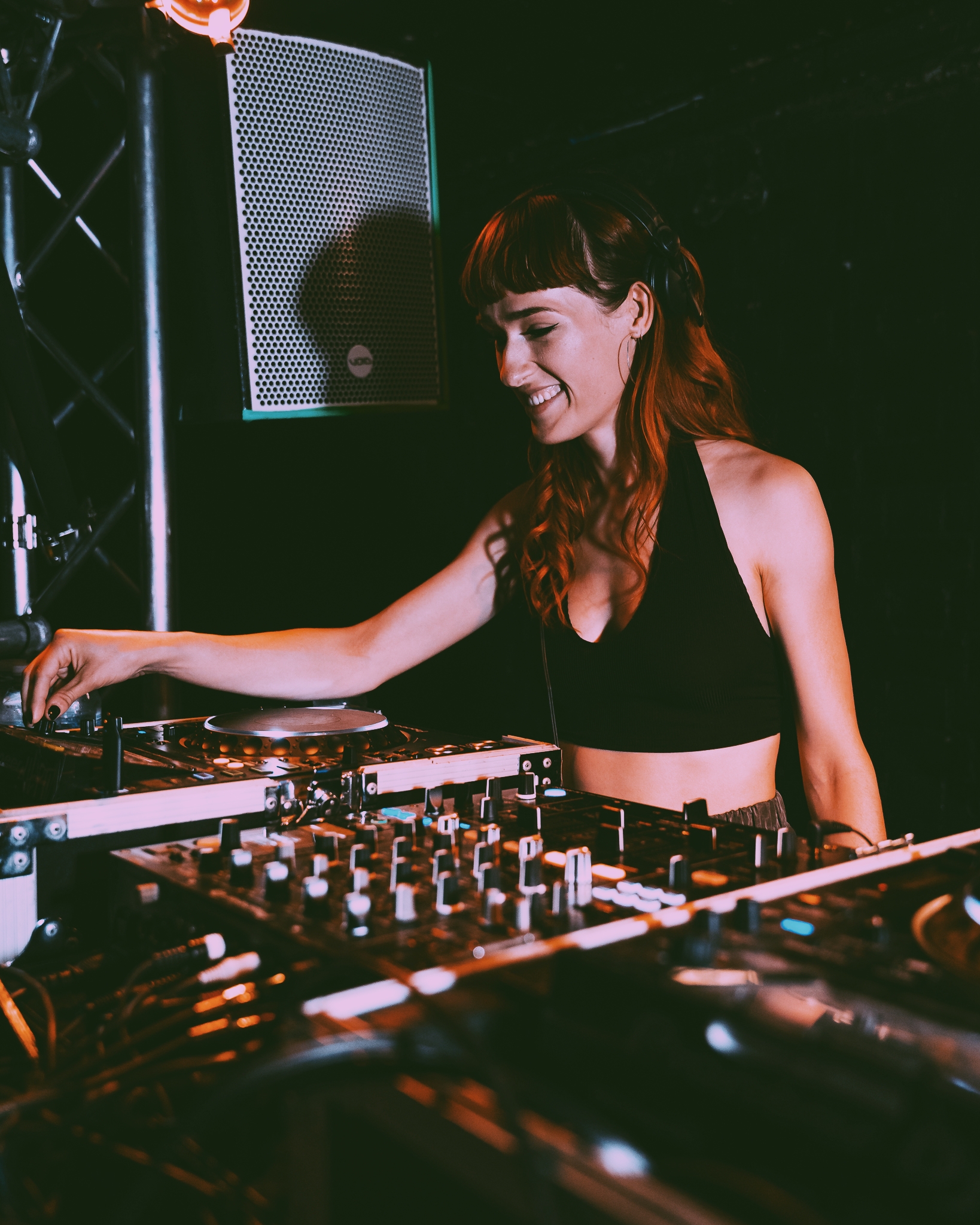 A DJ with warm lighting engages the crowd, surrounded by sleek turntables and vibrant audio equipment, creating an energetic atmosphere.