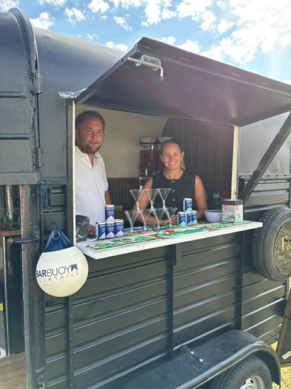 Stylish mobile cocktail van with black metal panels, clear martini glasses and branded cans on a neat white counter, bright daylight.