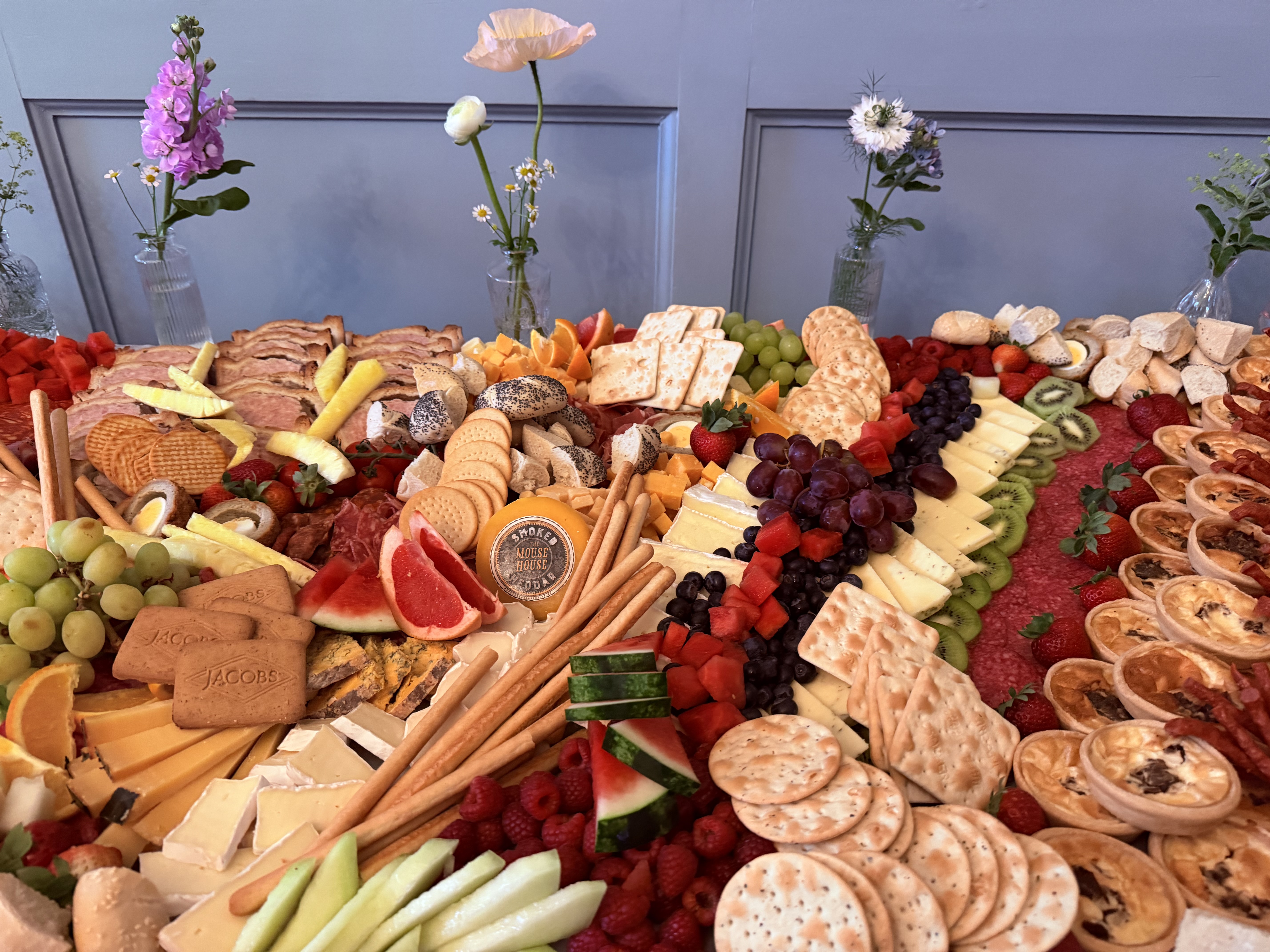 Vibrant cheese and charcuterie spread features figs, strawberries, salami, and crackers, all arranged artfully on a white tablecloth.