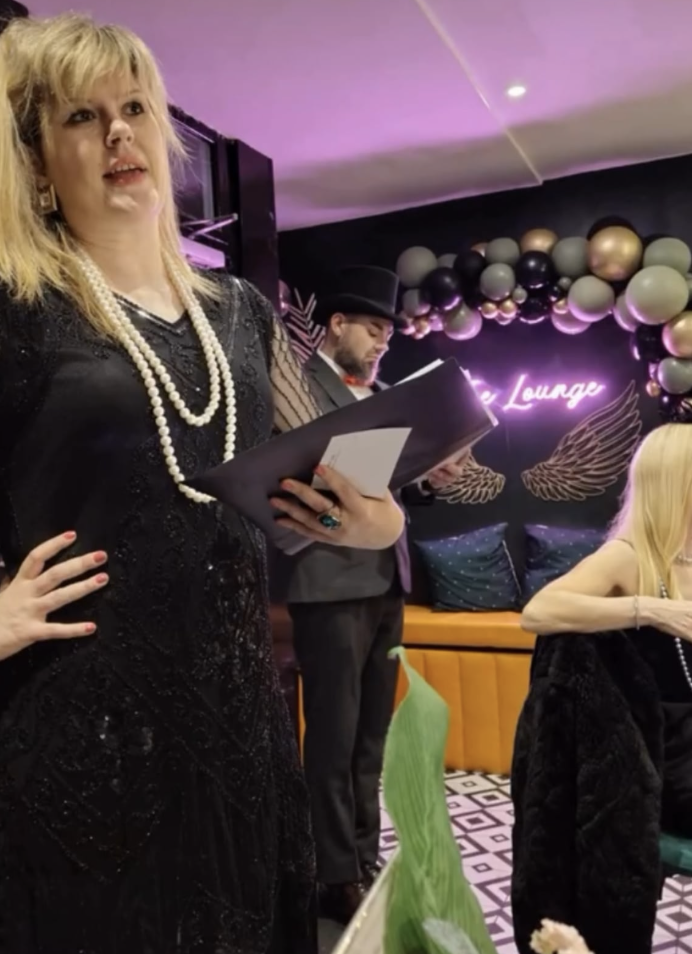 Stylish lounge event with black-and-gold decor, neon pink sign, balloon arch, and polished catering staff in warm, moody lighting.