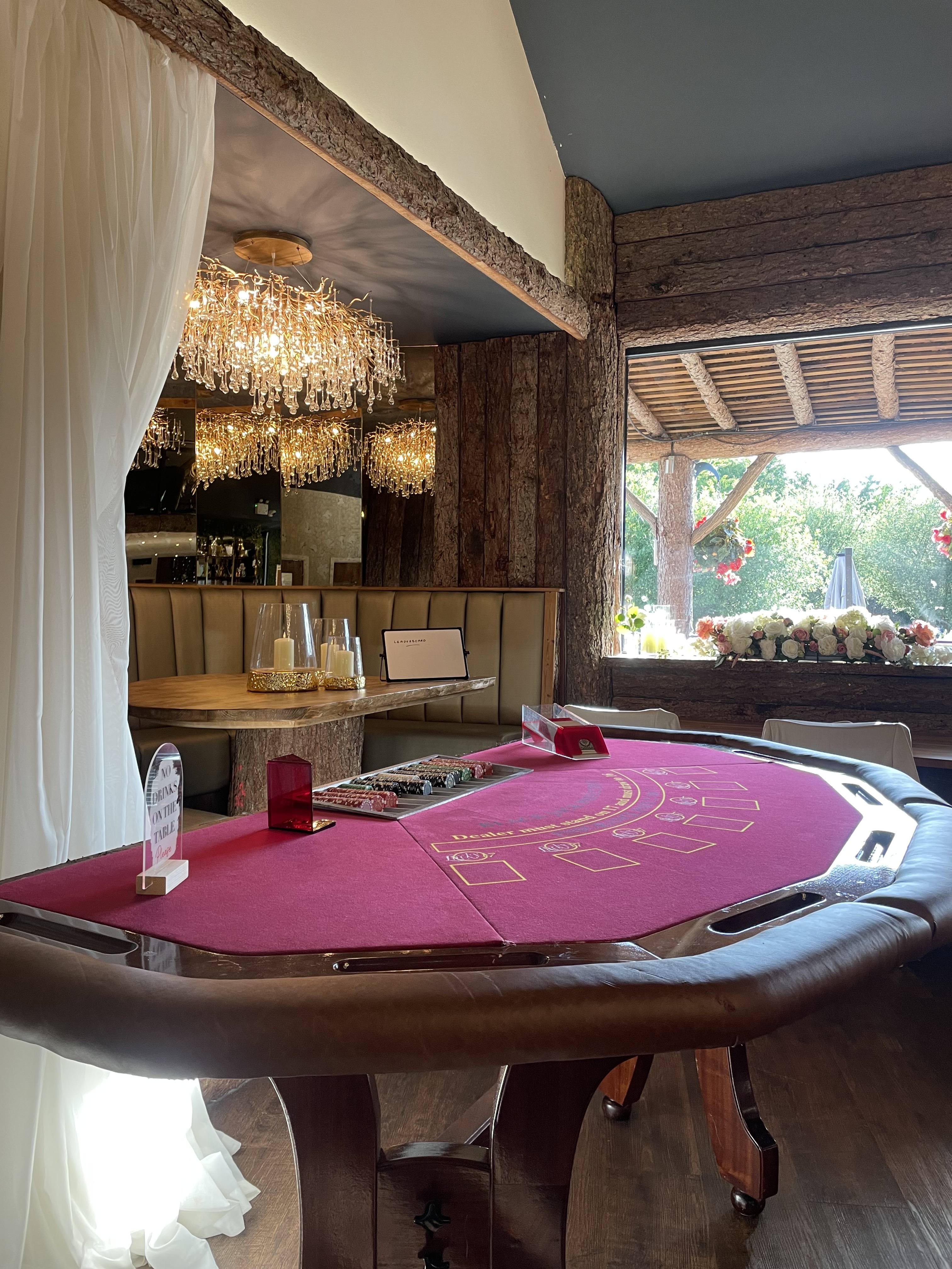 A polished wooden poker table with a vibrant red felt top displays stacks of chips and a card deck, framed by elegant mirrors and warm lighting.