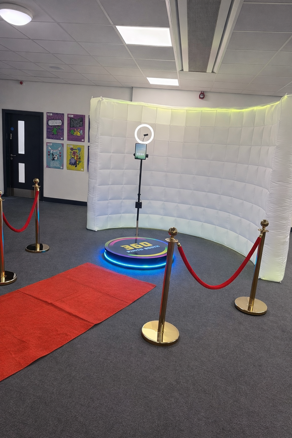 A sleek photo booth setup features a curved white backdrop, red carpet, and golden stanchions, creating a glamorous event atmosphere.