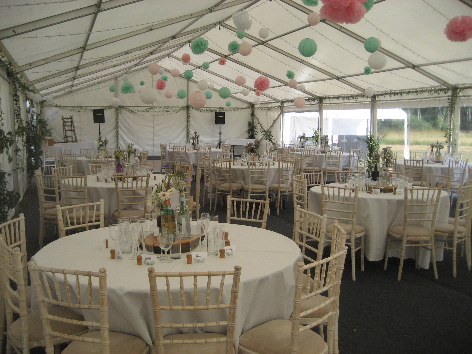 A spacious marquee features elegant round tables with crisp white linens, adorned with flowers, creating a charming atmosphere in soft daylight.