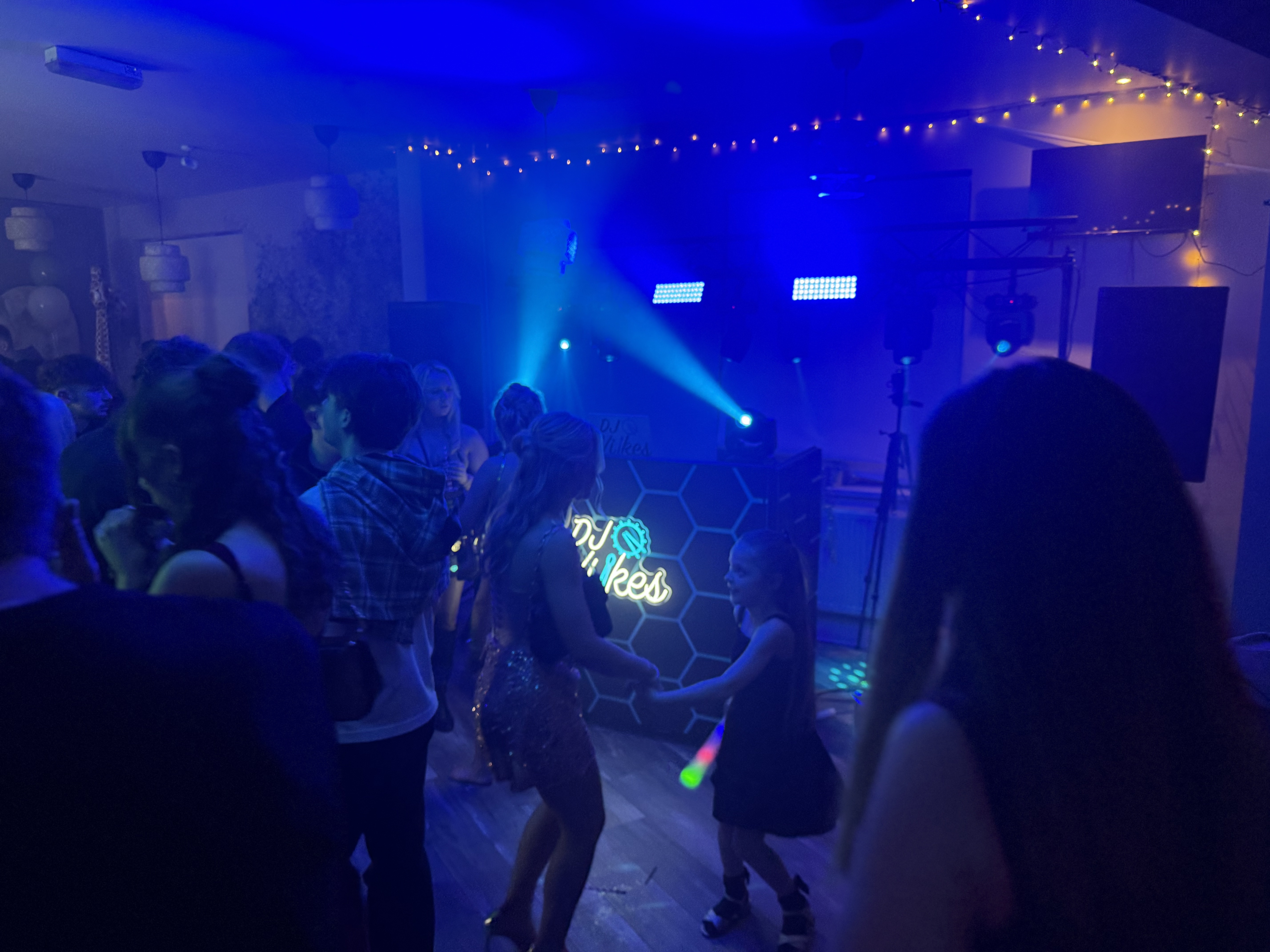 A vibrant party scene with blue lighting creates a festive atmosphere, while guests dance near a DJ booth featuring neon decor, enhancing service quality.