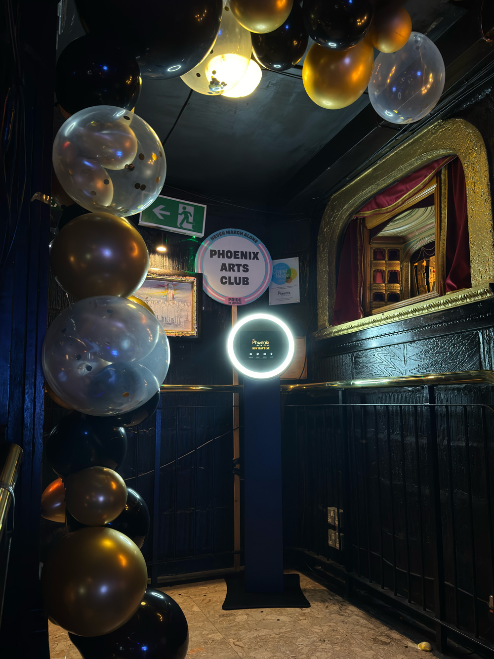 An ornate entrance featuring a glossy black wall adorned with a balloon arch in gold, black, and clear shades, evoking festive vibes.