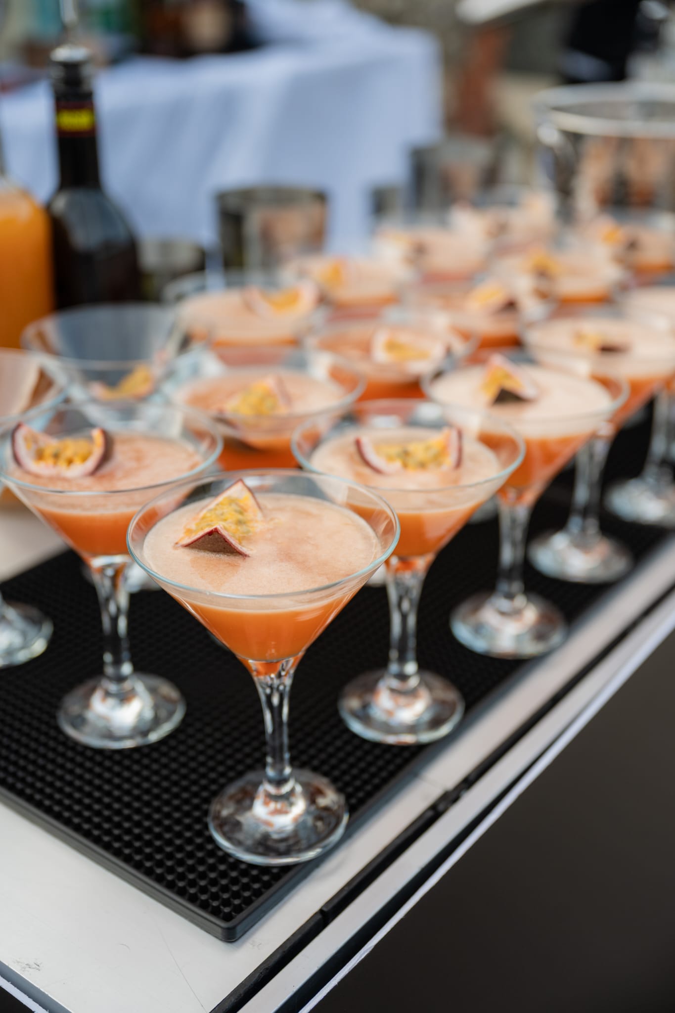 Elegant catering buffet with orange cocktails in martini glasses, neatly arranged on a black tray, bright daylight, polished service.