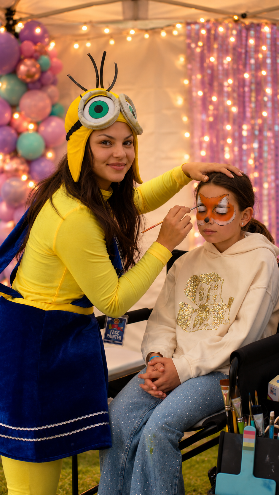 A smiling child shows off vibrant, glittery face paint featuring a wizard hat amidst pink and white starburst designs, exuding joy.