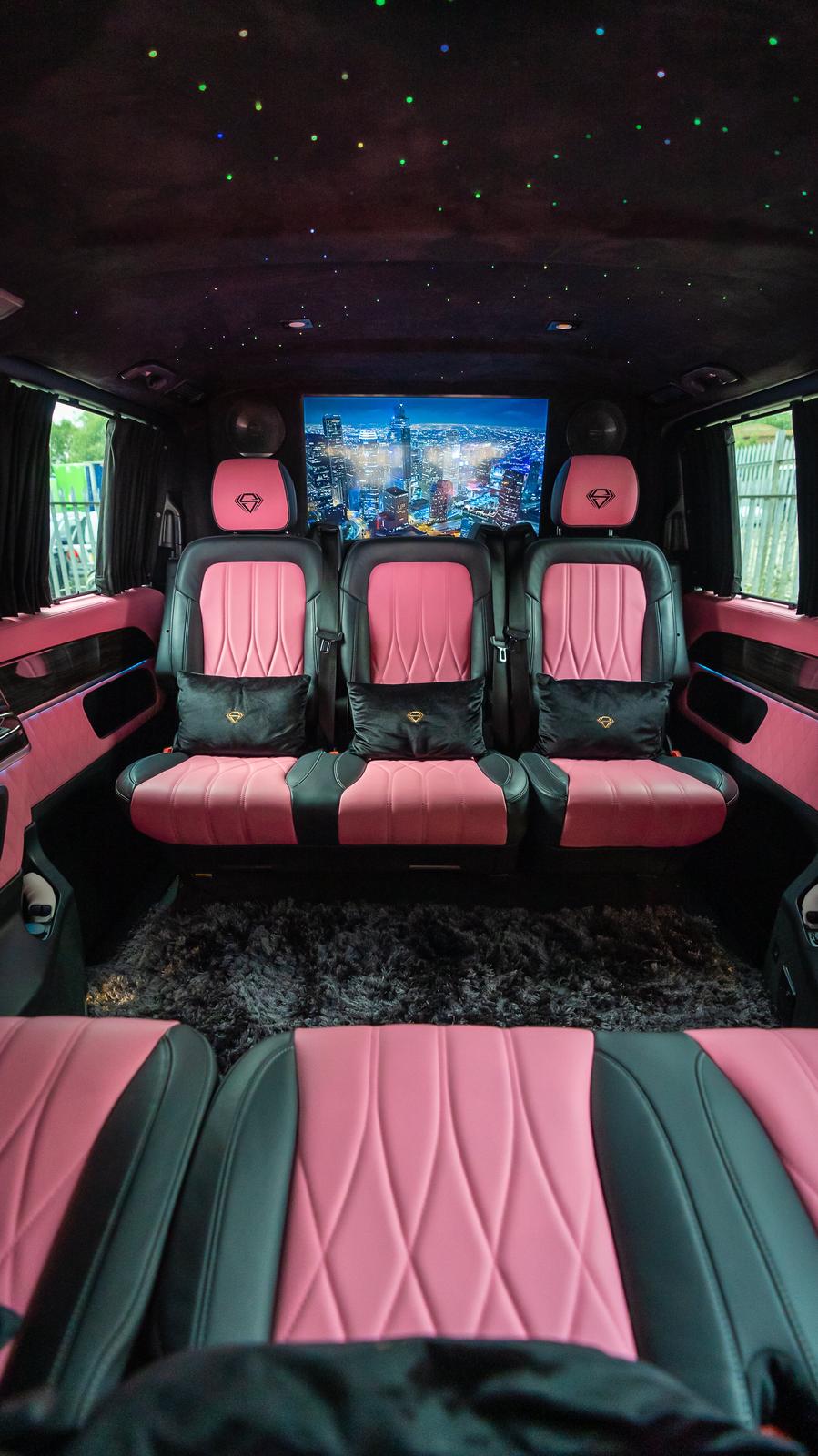 A luxury van interior features plush black and pink leather seating, ambient starry ceiling lights, and plush gray carpeting, exuding modern elegance.