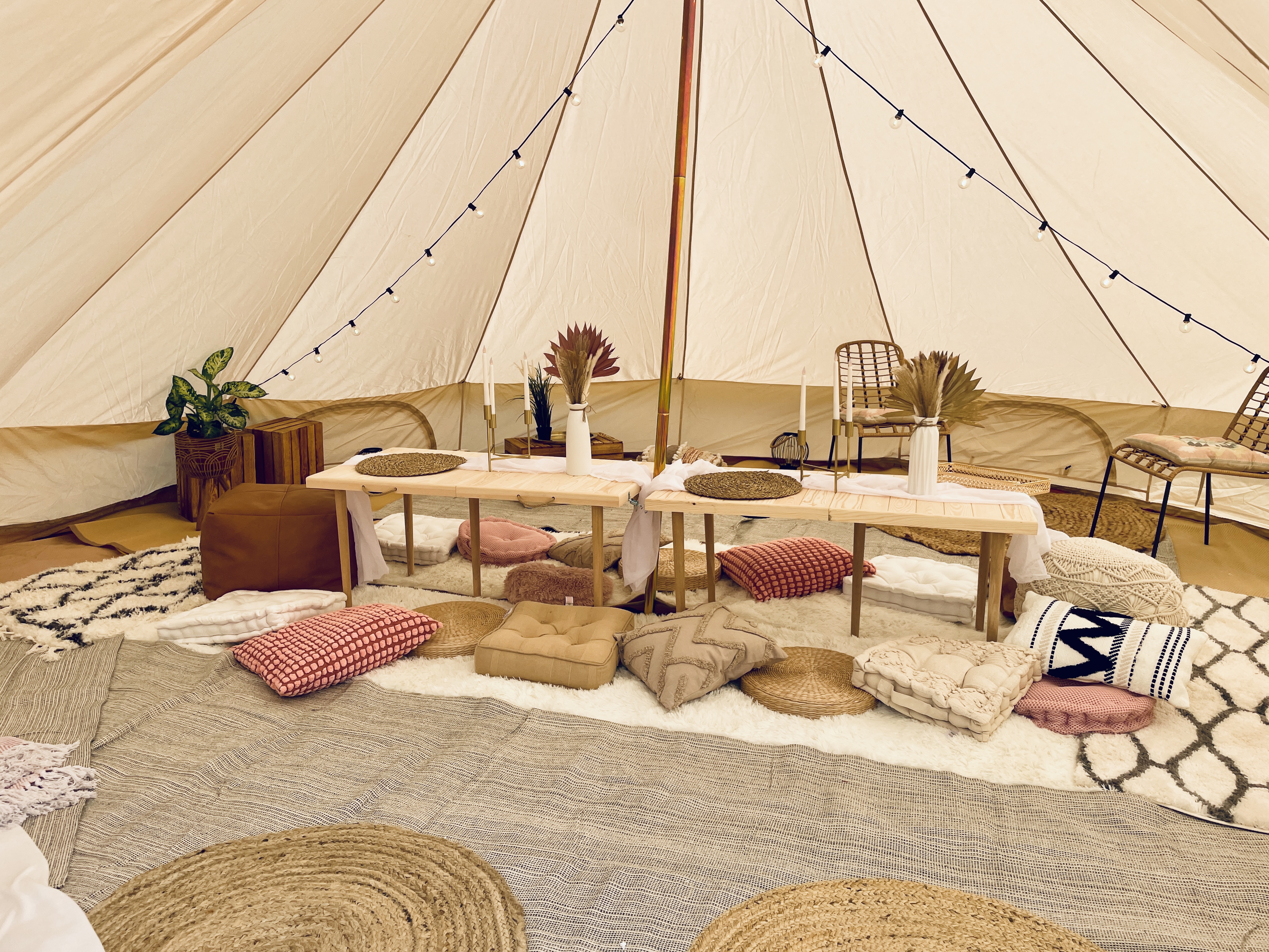 Inside a cozy tent, natural tones blend with textured cushions and woven mats; dim lights and rustic wood create an inviting atmosphere.