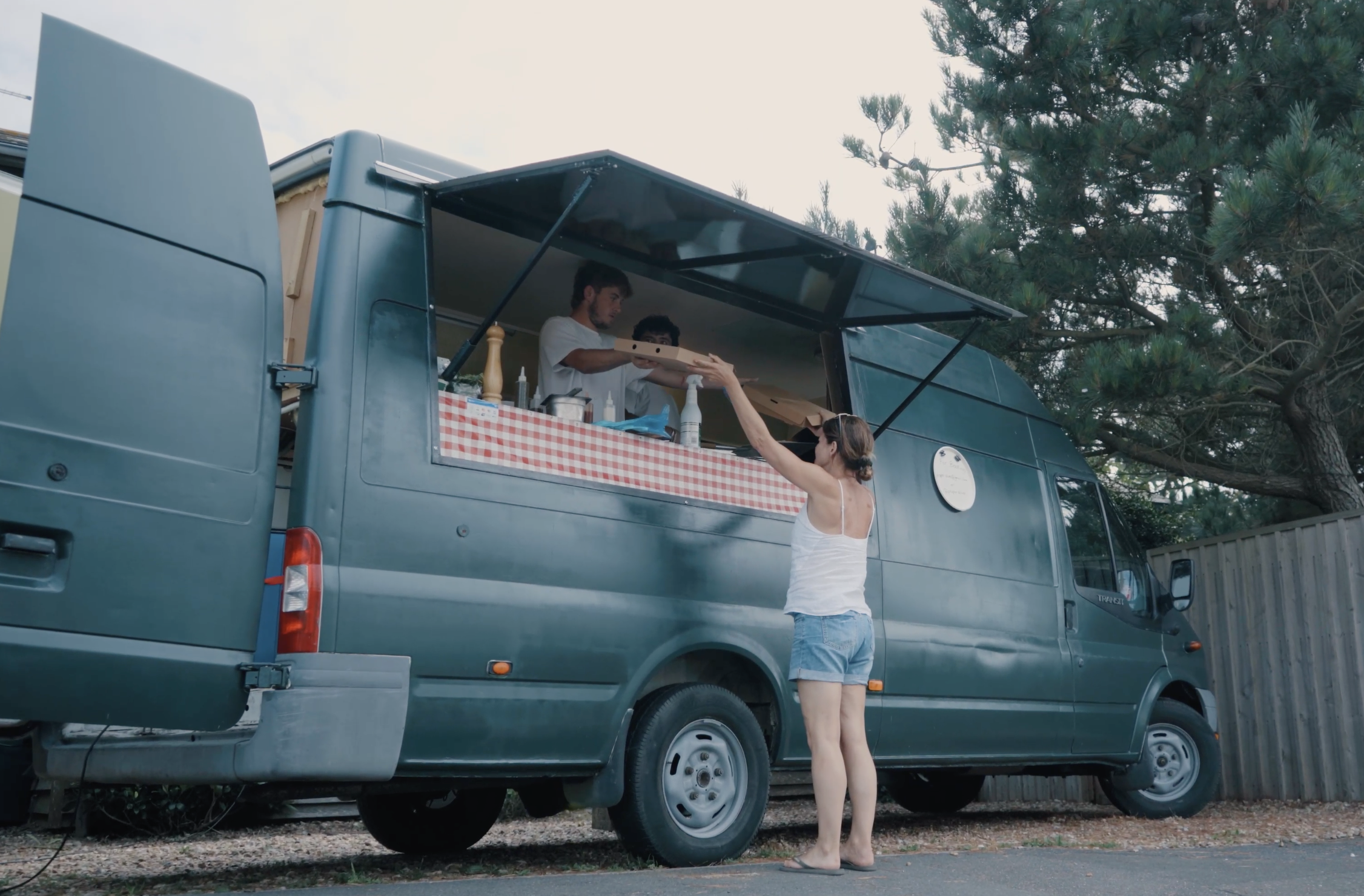 A charming food truck with a plaid tablecloth serves fresh dishes; a smiling woman interacts with the friendly staff outside.