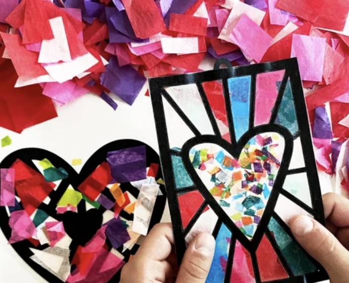 Vibrant stained glass crafts in bold pinks, reds, and purples, surrounded by colorful tissue paper. A playful, creative atmosphere.