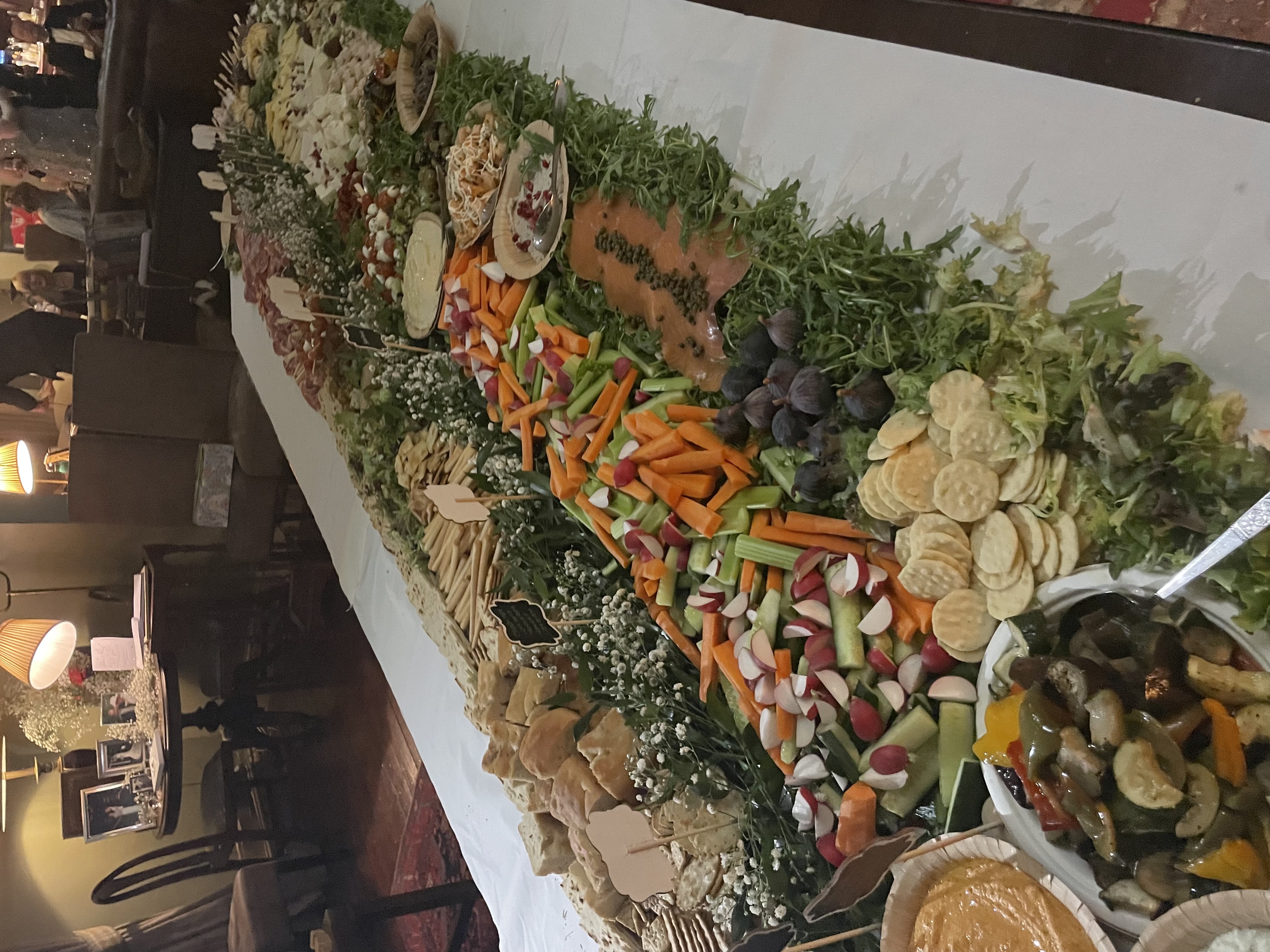 A vibrant spread of fresh veggies, artisan bread, and dips arranged meticulously on a white tablecloth, illuminated by soft lamp light.
