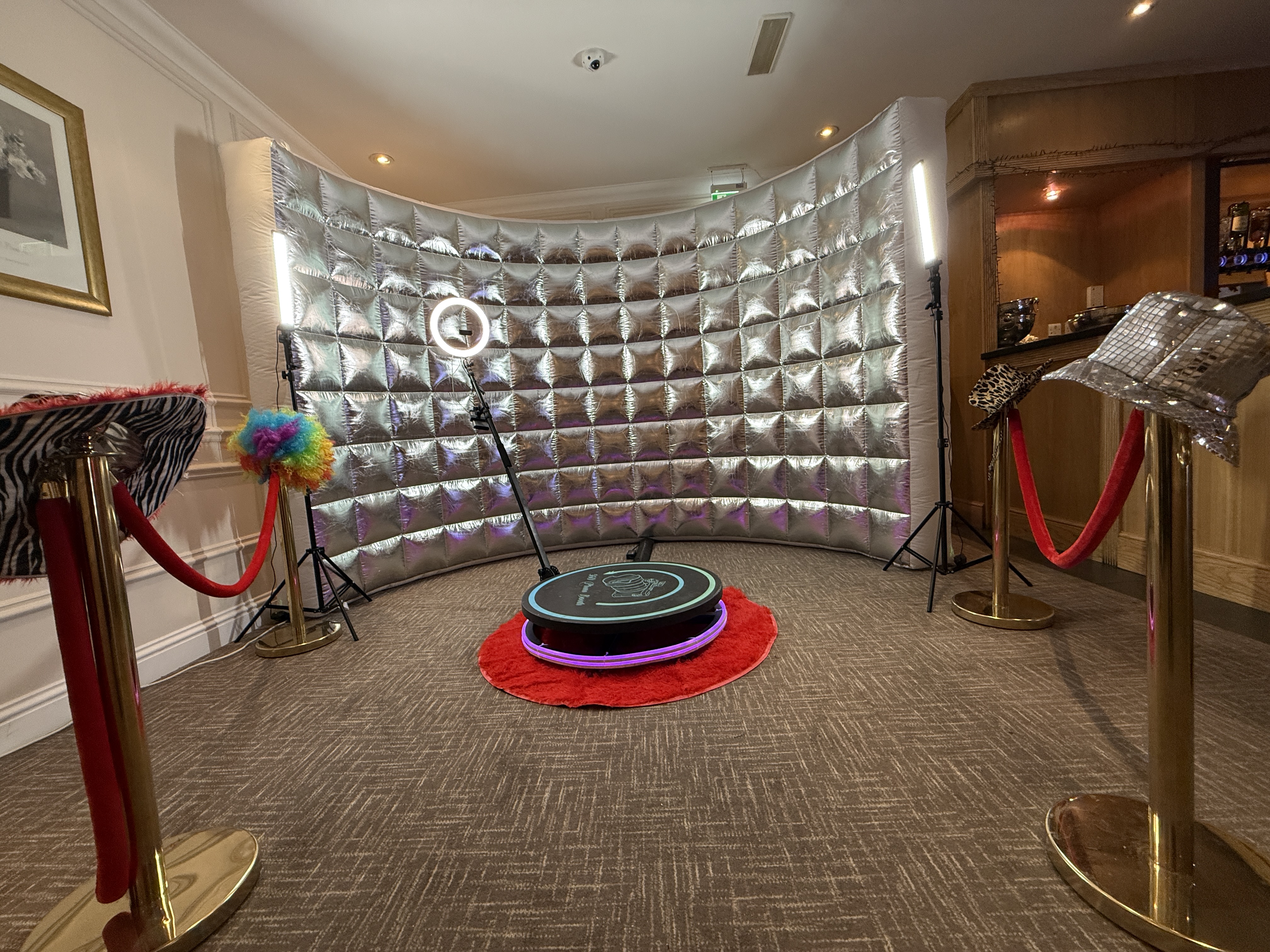 A vibrant photo booth setup features a metallic backdrop, bright ring lights, and plush red accents, creating a lively, glamorous atmosphere.