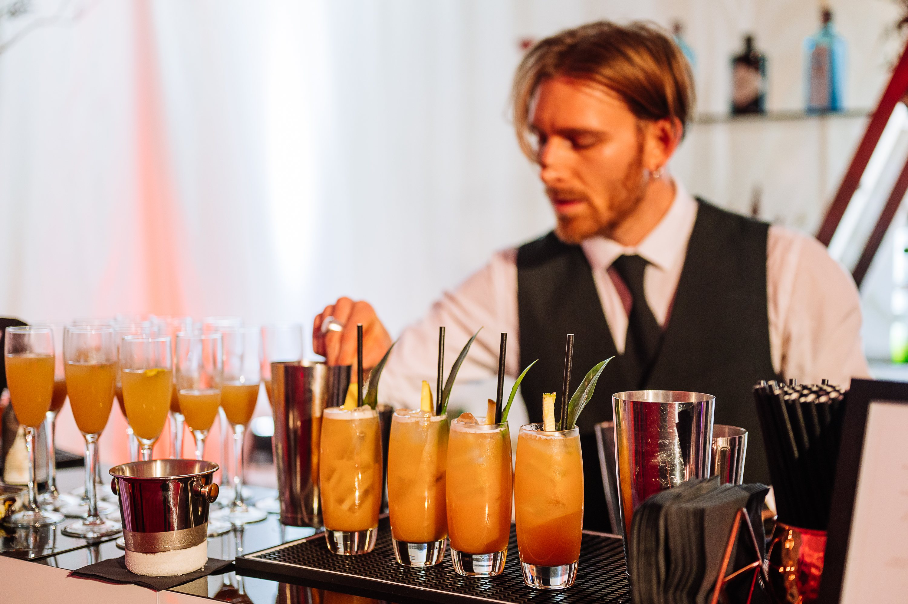 A stylish bartender prepares vibrant cocktails with fresh garnishes, surrounded by polished glassware and a sleek black bar, illuminated warmly.