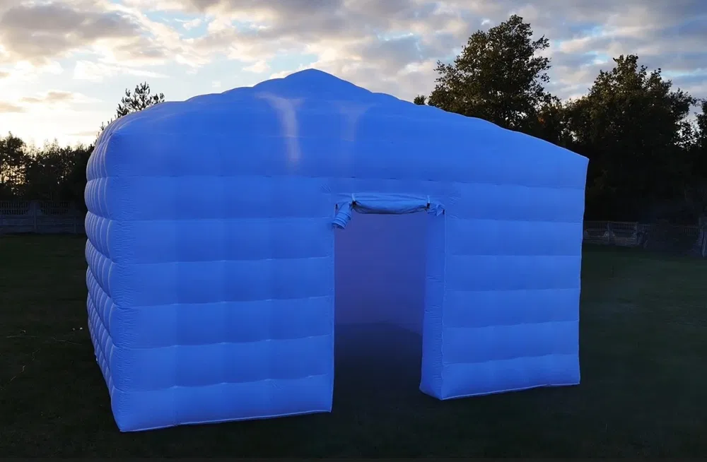 Blue inflatable event tent, softly lit at dusk on a grassy lawn, with a clean open doorway and sleek rental setup for catering.
