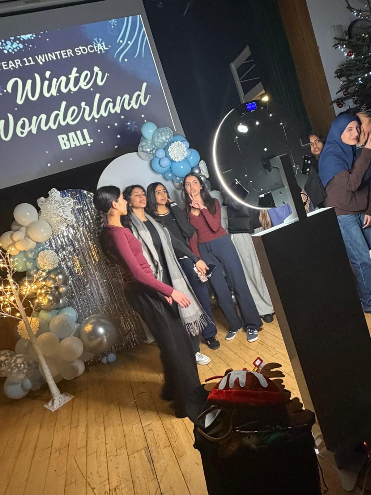 A joyful group, dressed in festive colors, poses under twinkling lights with a sparkling backdrop, embodying a cheerful Winter Wonderland vibe.