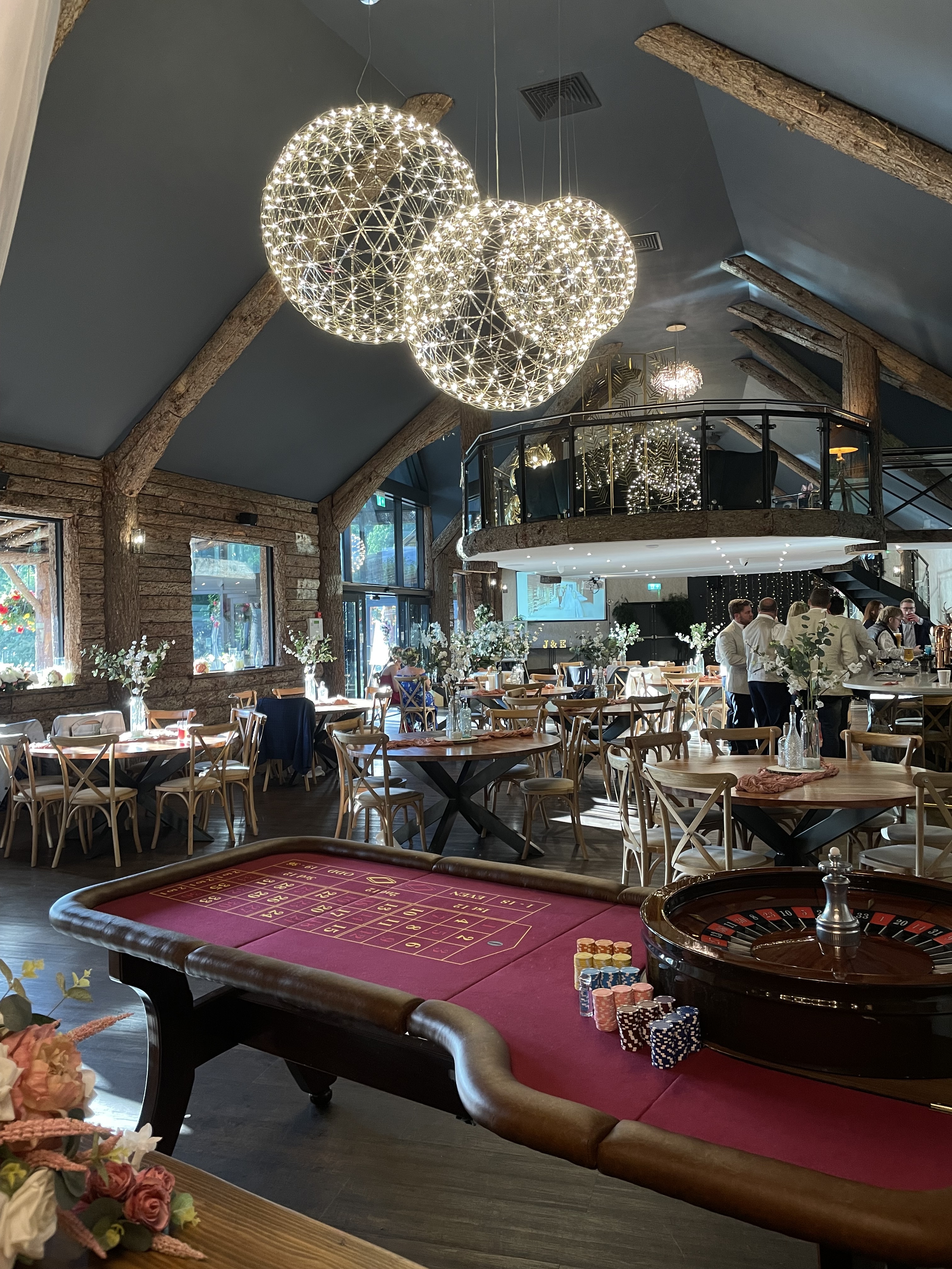 In a lively atmosphere, elegantly dressed women in black dresses and pearls engage around a red felt roulette table, vibrant chips nearby.