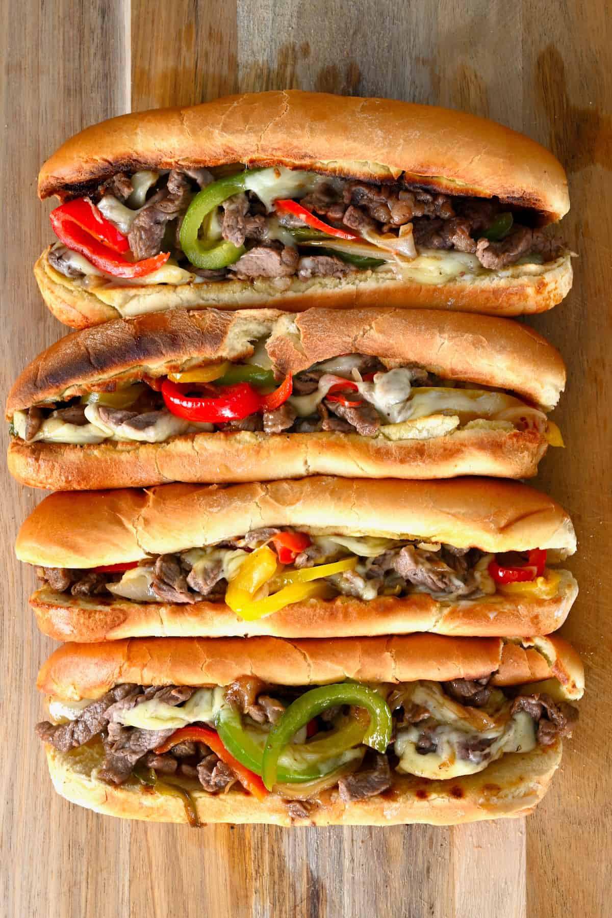 Stacked neatly on a wooden board, the savory cheesesteak subs feature melted cheese, grilled steak, and vibrant bell peppers.