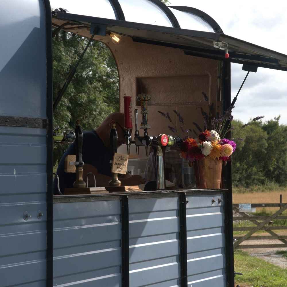 A charming vintage bar van displays polished taps and a vibrant bouquet, set against a sunny outdoor backdrop, inviting casual gatherings.