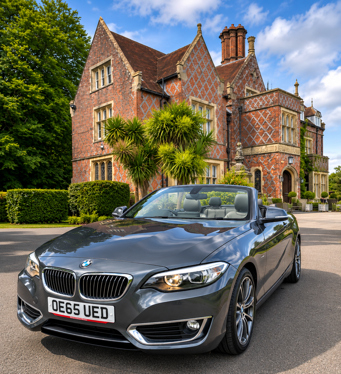 A sleek gray BMW convertible sits before a grand red-brick manor, polished and sunlit, evoking luxury chauffeur service and event transfer.