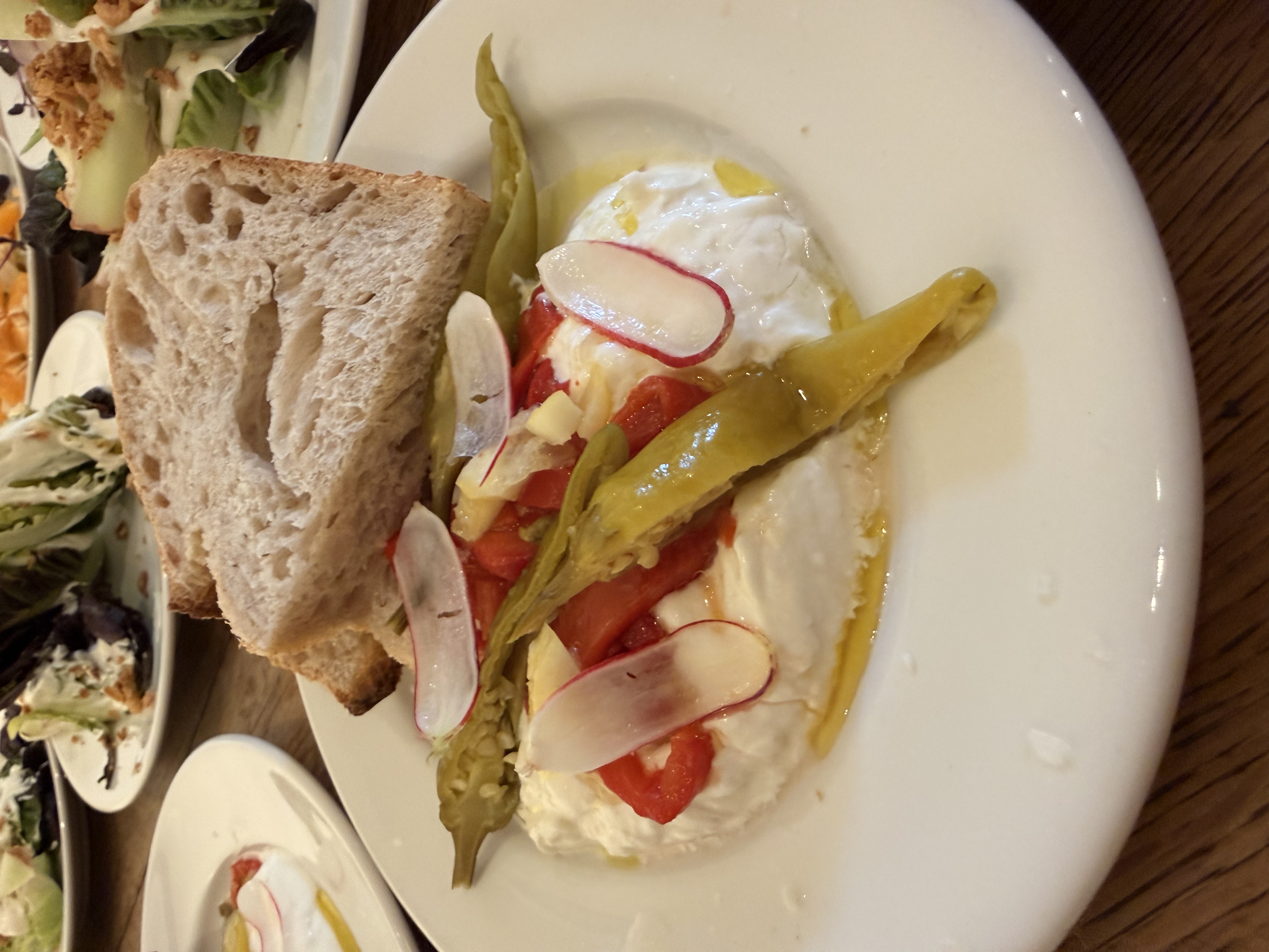 Artful catering plate on wood table: burrata, roasted peppers, pickled radish, asparagus, rustic bread, softly lit buffet elegance.