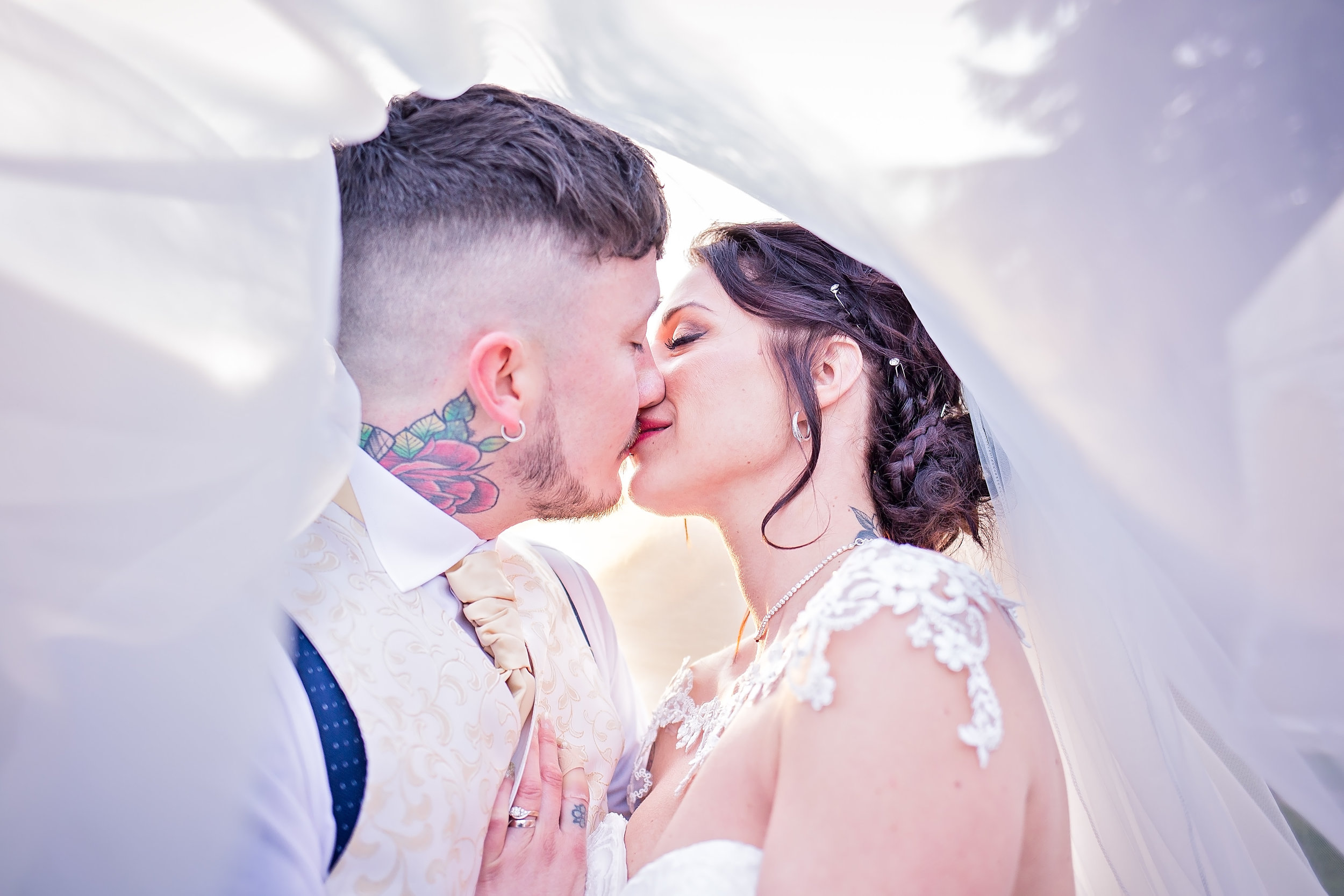 A couple shares a tender kiss, framed beautifully by soft, flowing fabric; their elegant attire and intimate atmosphere radiate love and warmth.