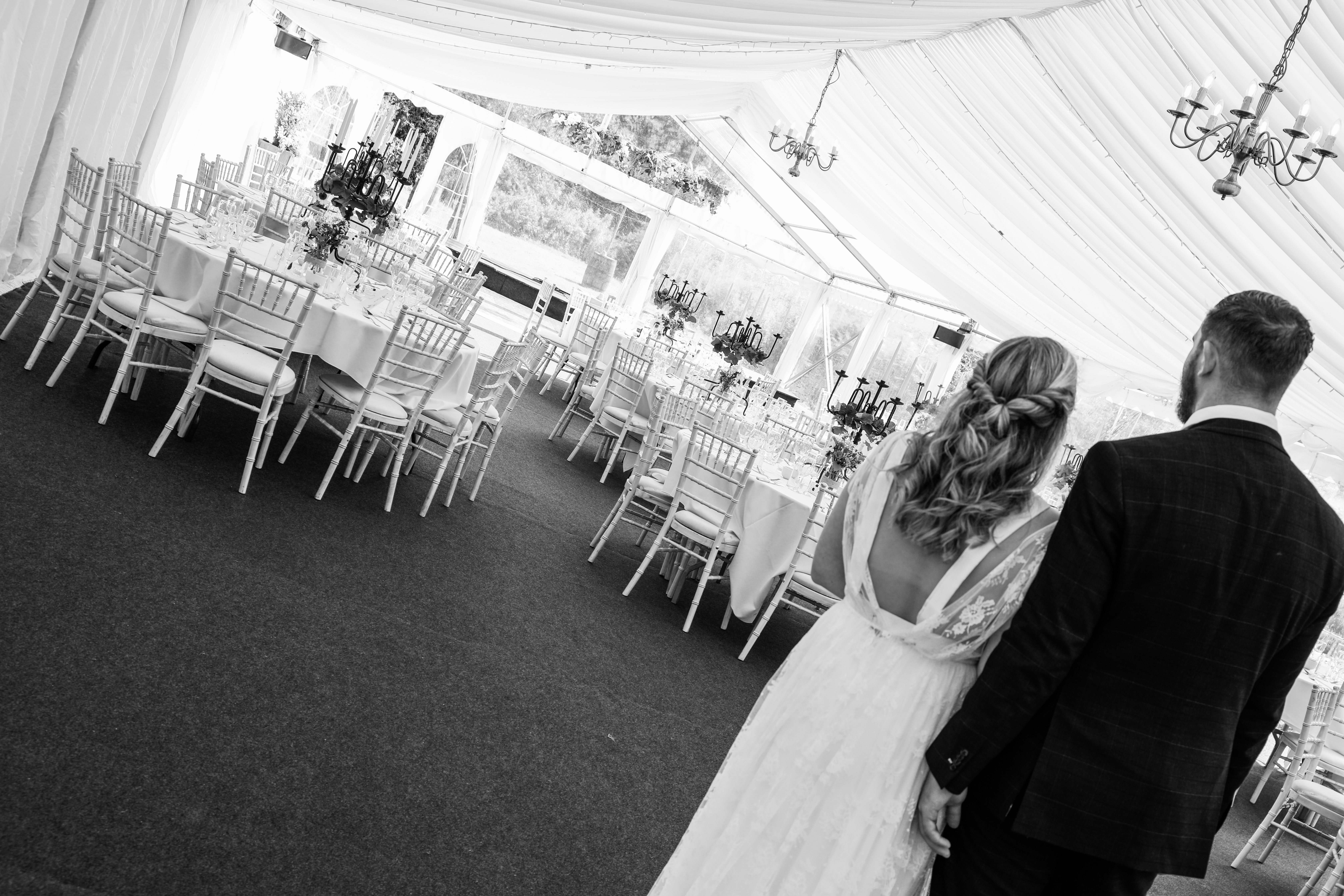 A beautifully arranged reception space features round tables with crisp white linens, elegant candelabras, and polished glassware, under soft daylight.